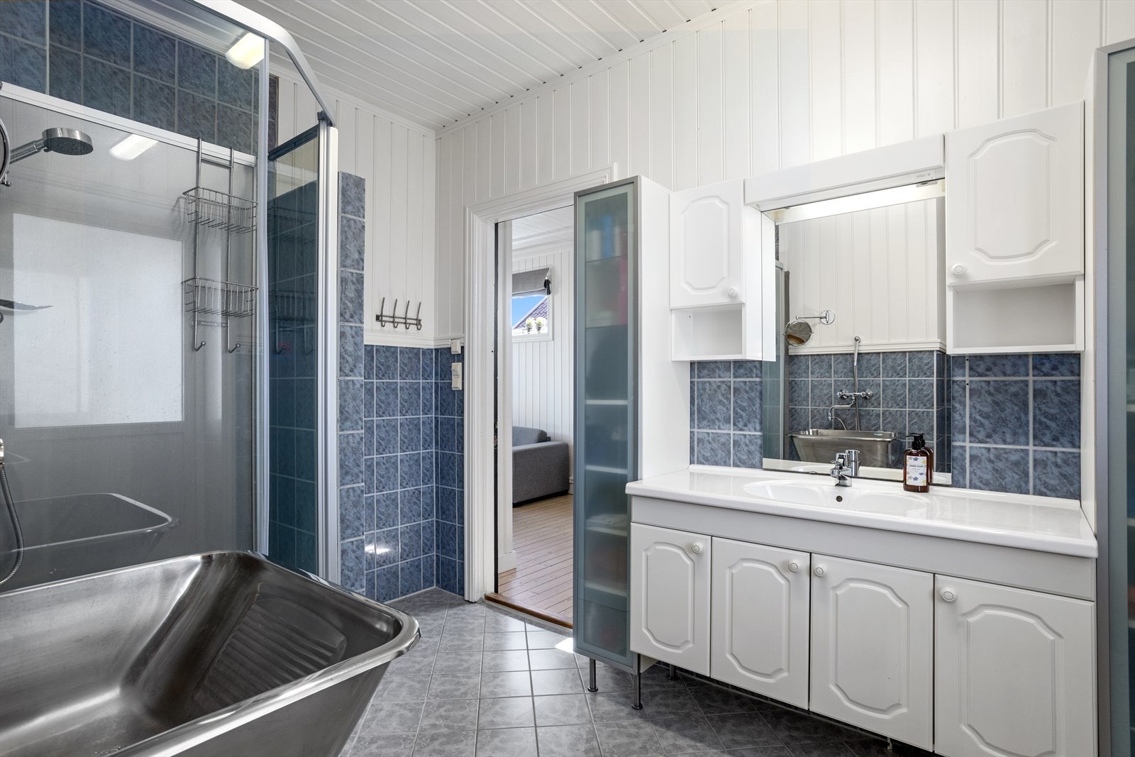 Stort bad med flis på gulv og vegger, enkelte vegger med brystpanel over flis. Det er malt panel i tak. Det er varmekabel i gulv. Badet har sanitærutstyr som toalett, dusjkabinett og vask. Galleribilde