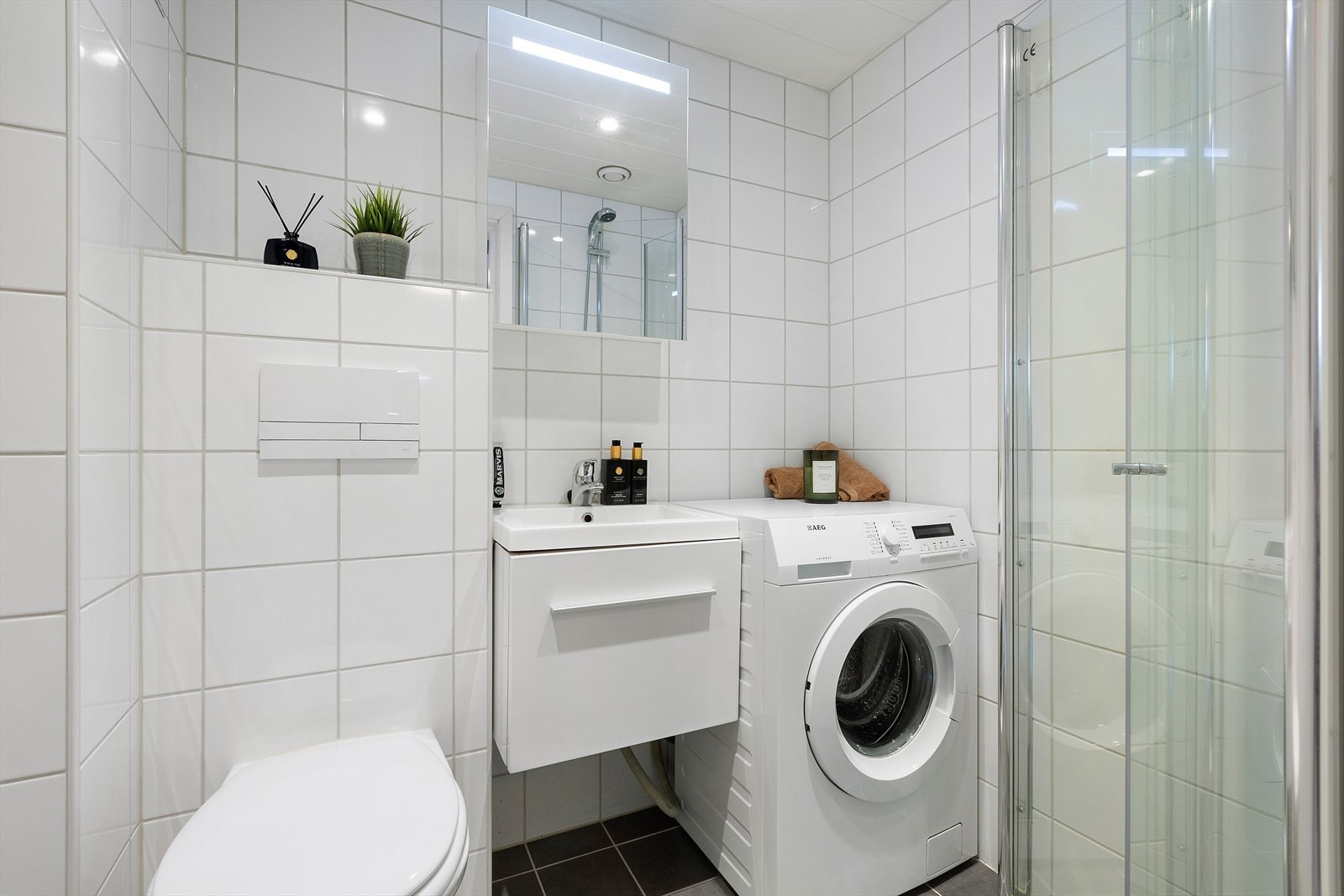 Flislagt baderom med varmekabler i gulv. Badet er fra 2014 og inneholder nedfelt servantinnredning med speil, vegghengt toalett, dusjhjørne med dusjvegger og opplegg for vaskemaskin. Galleribilde