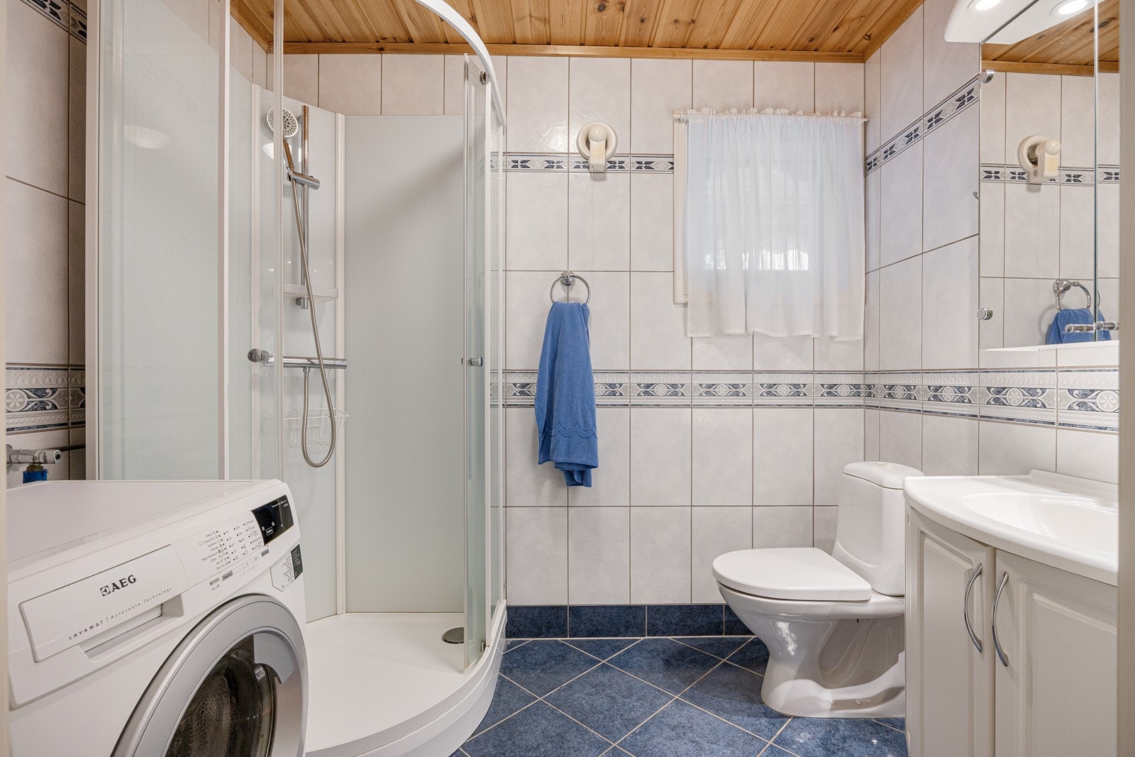 Badet er innredet med hvite veggfliser og mørkeblå gulvfliser. Galleribilde