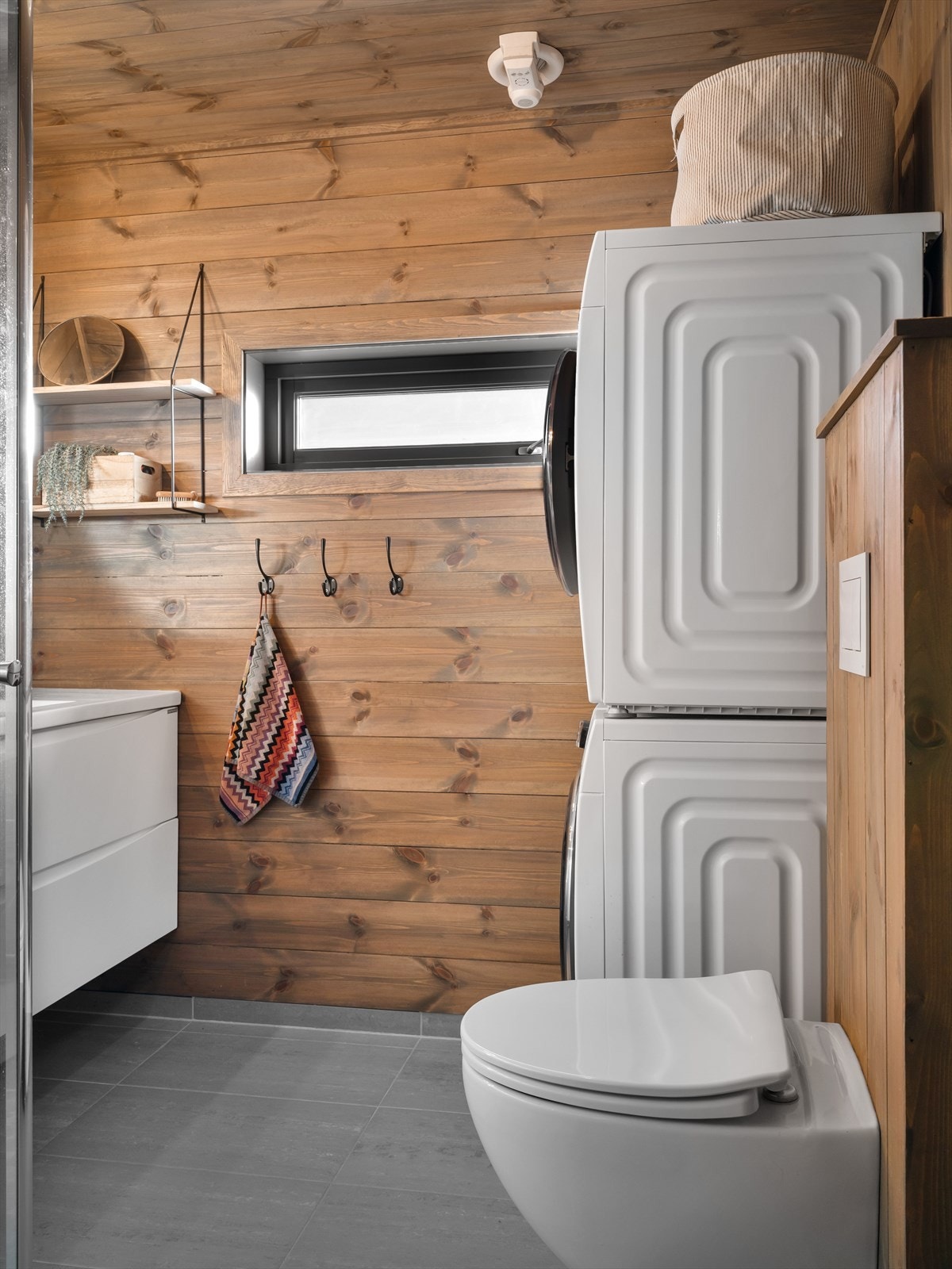 På badet finner du dusjhjørne, vegghengt toalett og vaskseksjon. Her slipper du å ta med skittentøyet hjem, da det er mulighet for både vaskemaskin og tørketrommel på hytten. Lunt hyttebad med delikat panel på vegger utenfor våtsone. Galleribilde