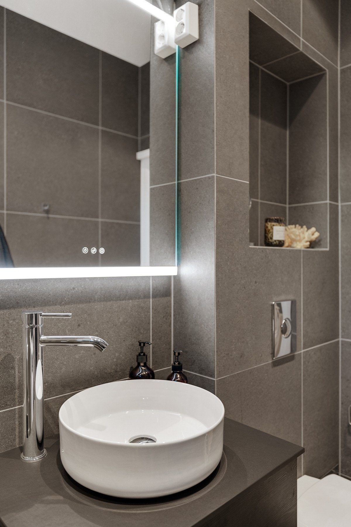 Badet inneholder vegghengt innredning fra 2023 med ovenpåliggende servant, speil med overlys, vegghengt toalett og dusjhjørne med innfellbare dører. Galleribilde