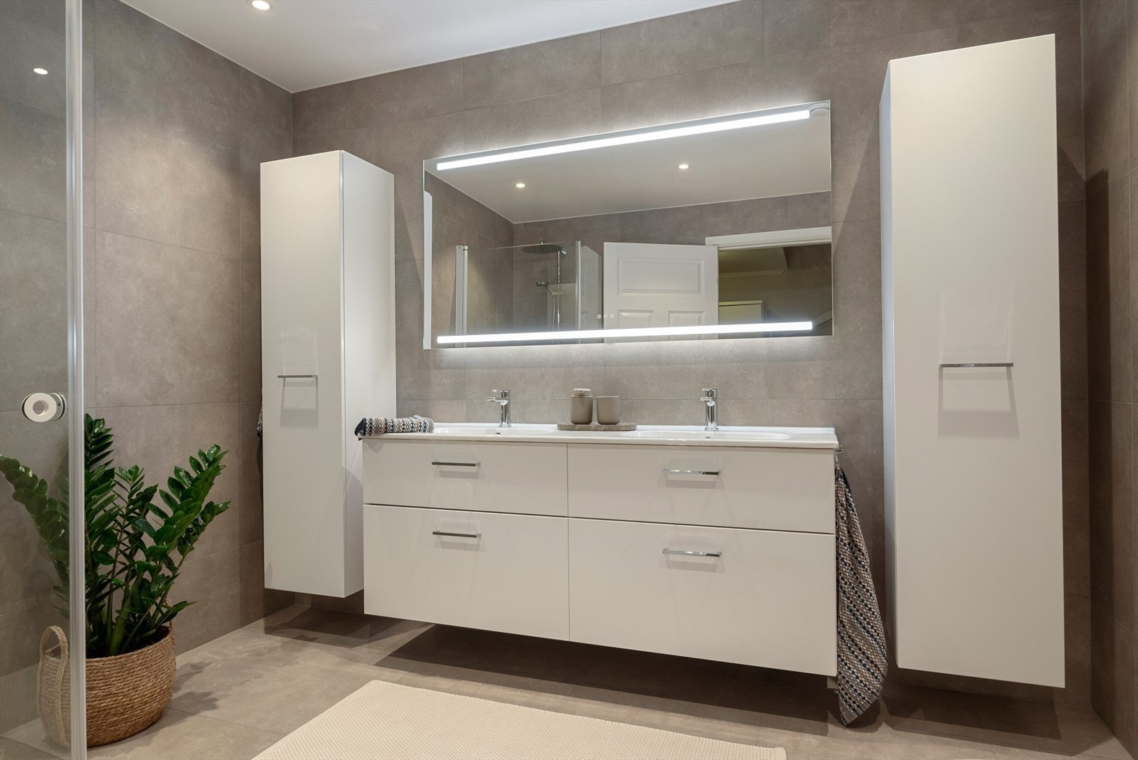 Badet er lyst og innbydende, med fliser på gulv og vegger, samt gulvvarme og downlights som gir ekstra komfort. Galleribilde