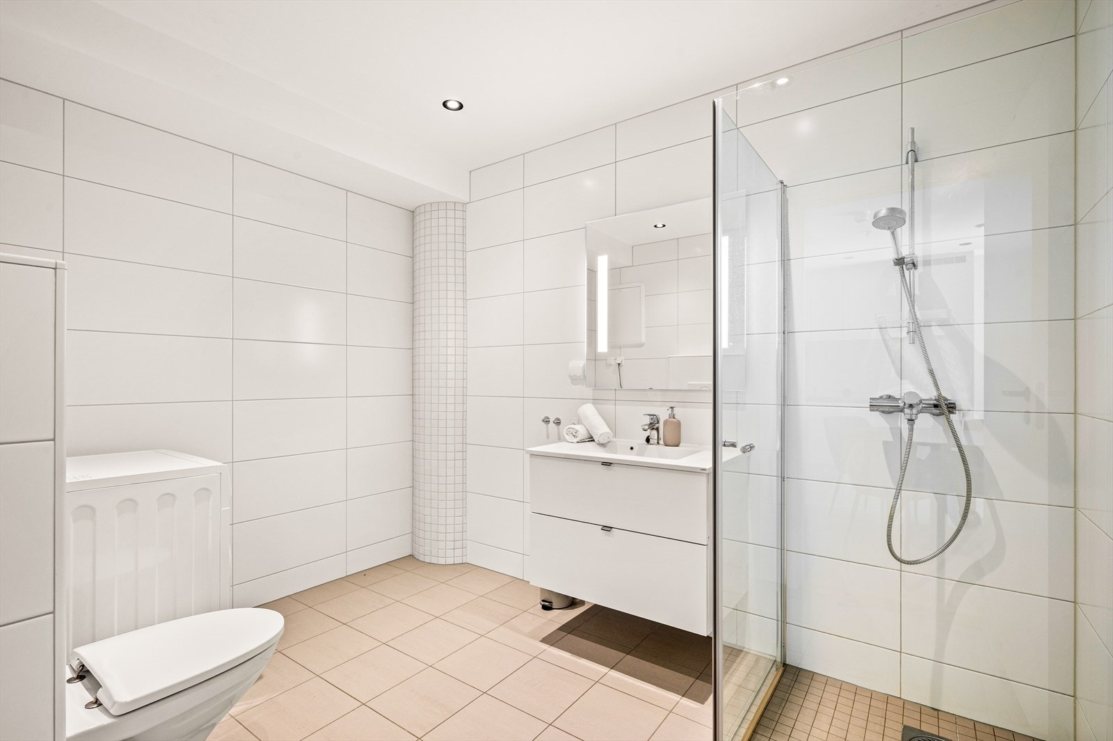 Baderommet er helfliset og har nydelige spotter i taket. Her er også servant med skuffeseksjoner, vegghengt toalett med, vegghengt speil med integrert belysning, samt stort dusjhjørne med glassvegger i. Det er opplegg for vaskemaskin og tørketrommel. Galleribilde