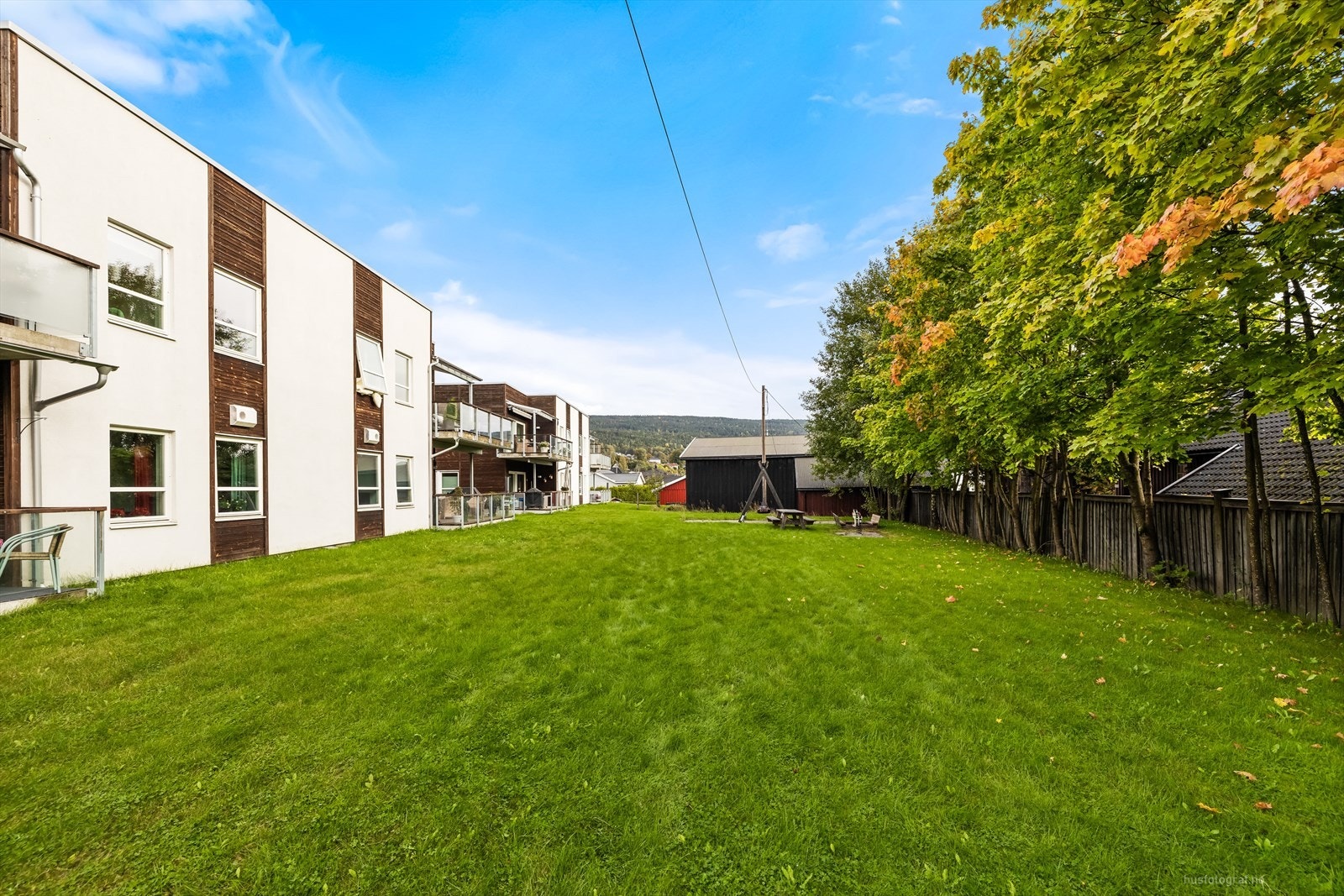 Felles eiet tomt som er pent opparbeidet med stor gressplen, beplantinger og avgrenset med hekk. Lekeplass med huskestativ. Galleribilde