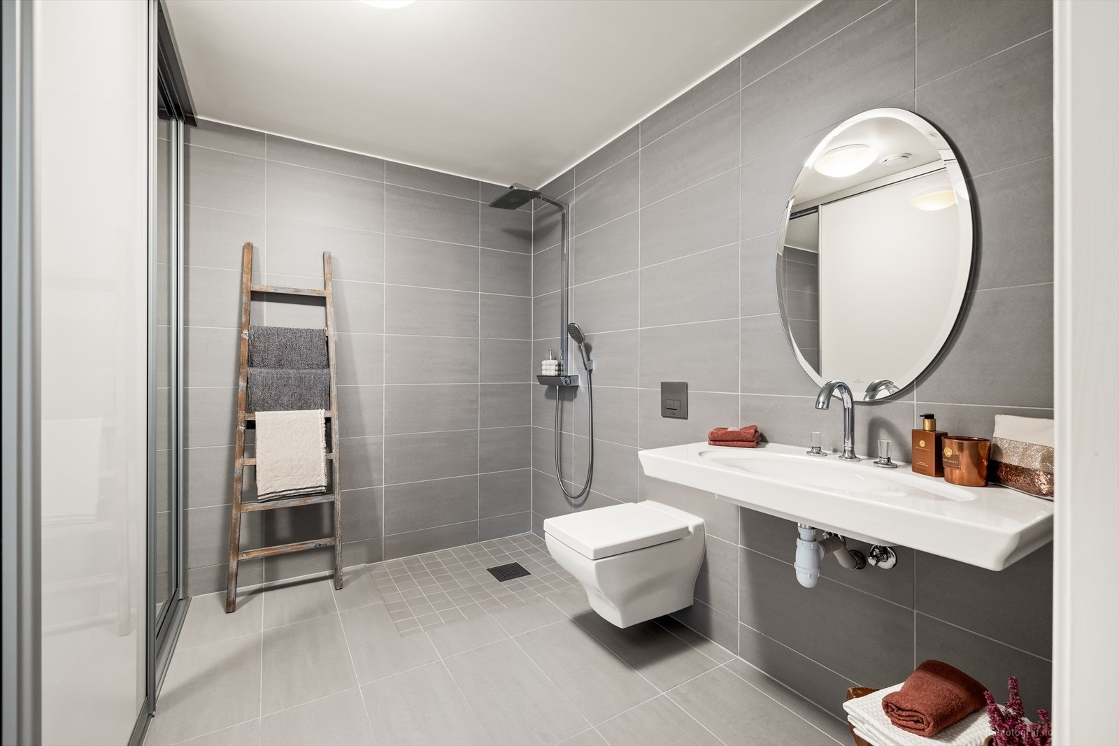 Badet har flislagte overflater, vegghengt toalett, dusjhjørne, servant og speil. Galleribilde