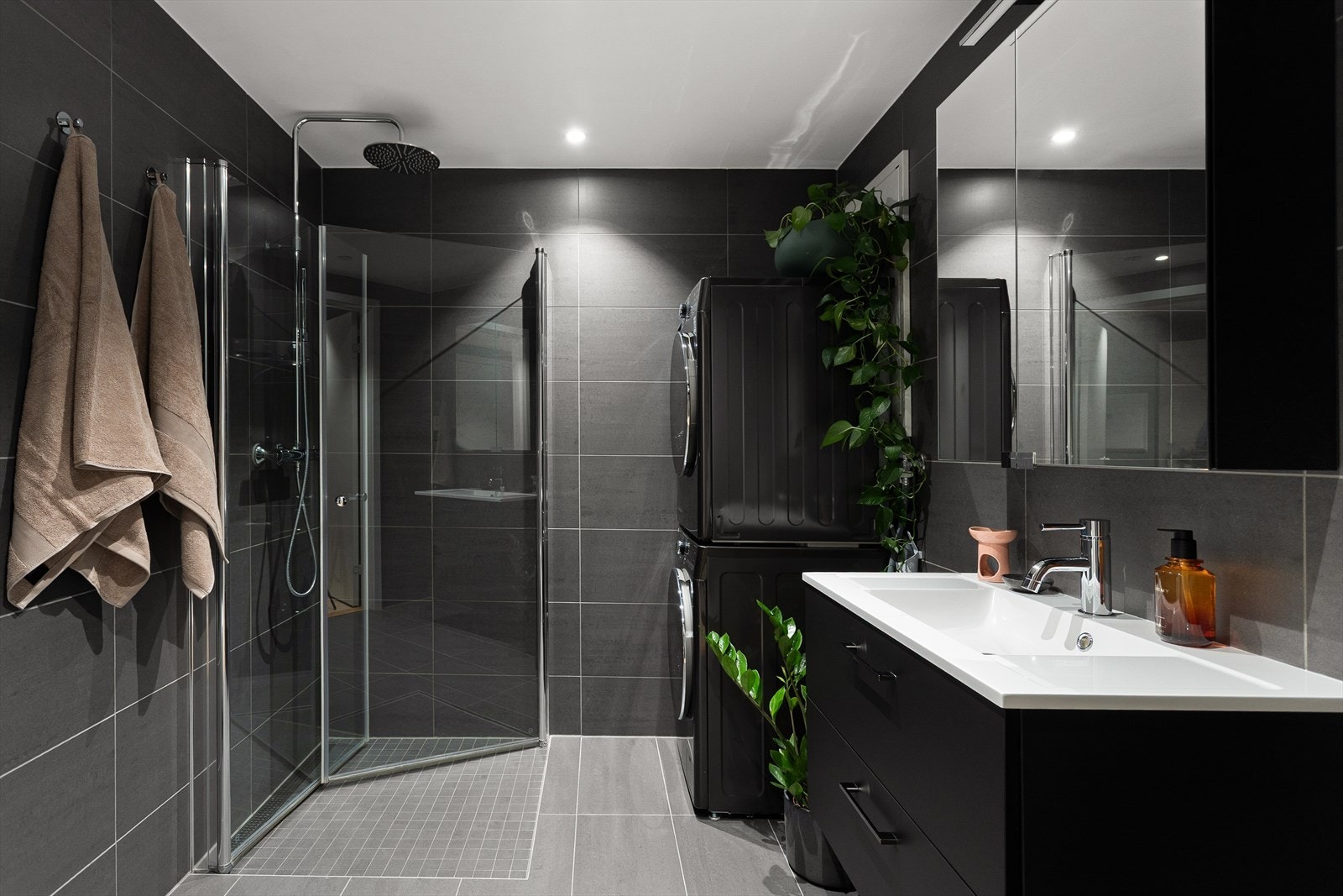 Badet er delikat med mørke fliser og er innredet med dusjhjørne, vegghengt toalett og baderomsinnredning med heldekkende servant, skuffer og speil. Galleribilde