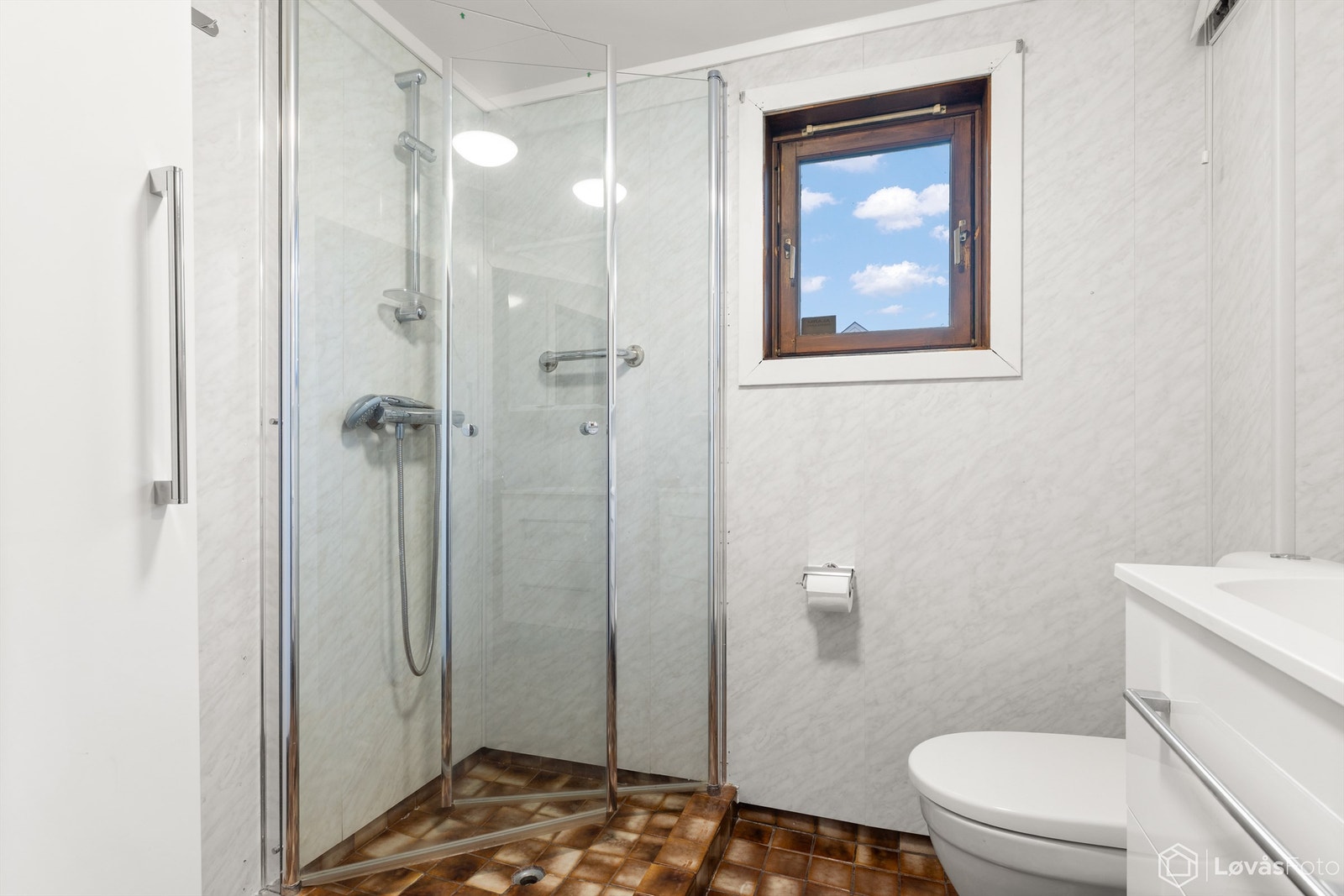 Rommet er utstyrt med vegghengt servantinnredning med skuffer, heldekkende servant og ett-greps armatur, speilskap med overlys og stikkontakt, dusjhjørne med glassdører og to-greps armatur, samt frittstående toalett. Galleribilde