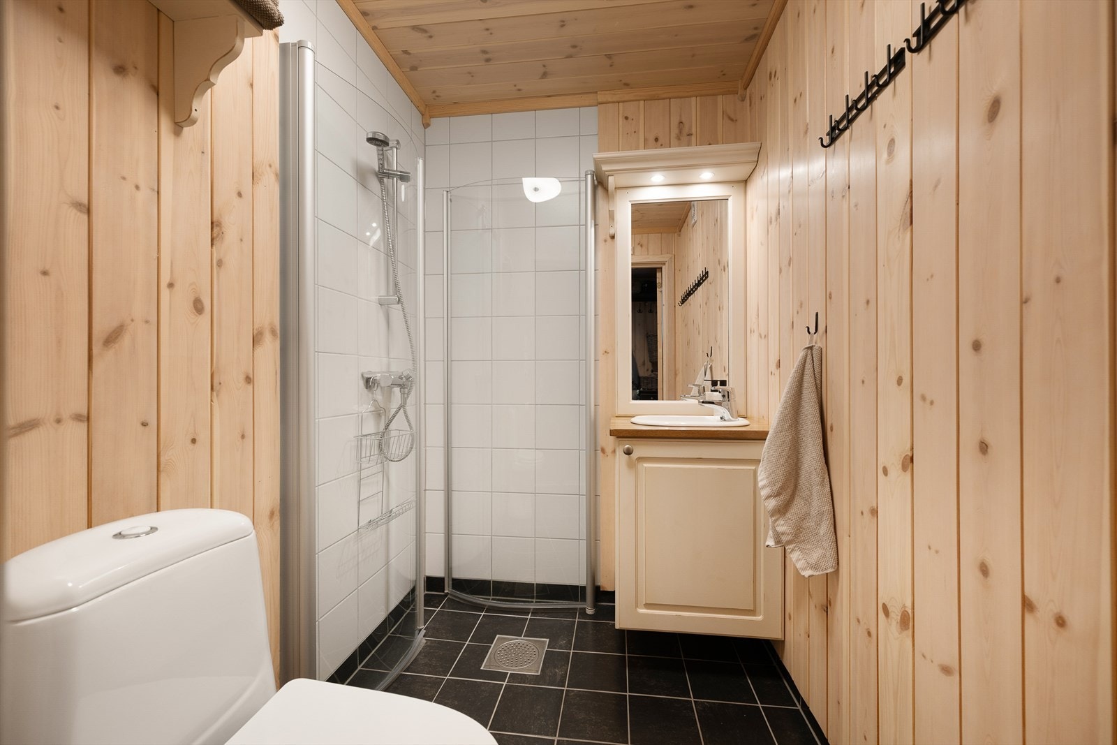 Gjestebadet har dusj med innfellbare glassdører. Enkel servant i innredning og gulvmontert WC. Galleribilde