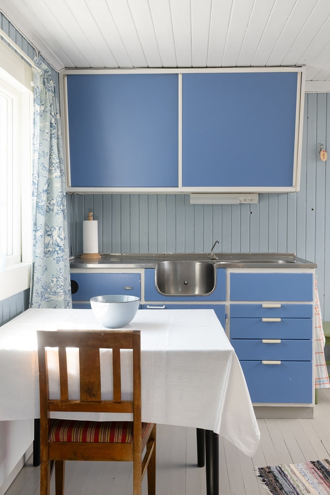 Overskap med skyvedører og enkel kjøkkenbenk med skuffesekjon. Fin plass til kjøkkenbordet under vinduet. Galleribilde