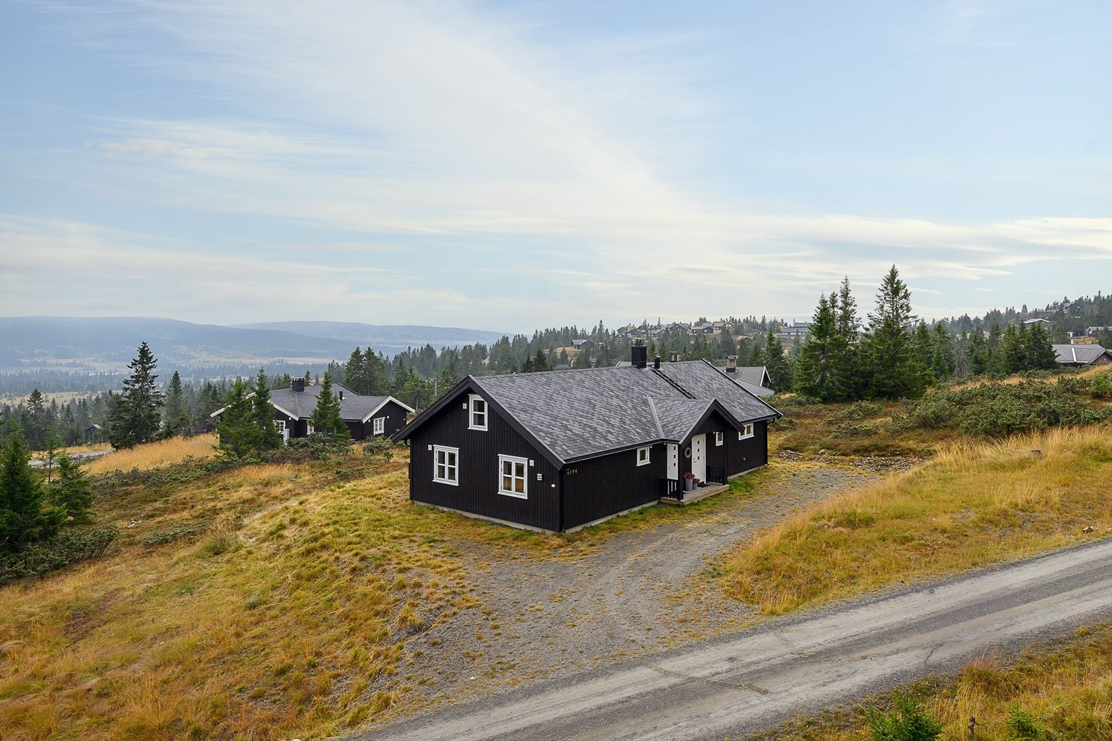 Gruset adkomst og biloppstillingsplass utenfor hytta. Eiet tomt, etablert område. Galleribilde