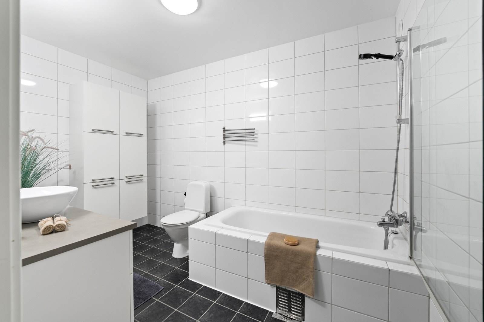 Bad. u.etg. Innfliset badekar med dusj med innfellbar dør i herdet glass. Servant og klosett. Veggskap med glatte fronter. Speil og belysning over servant. Galleribilde