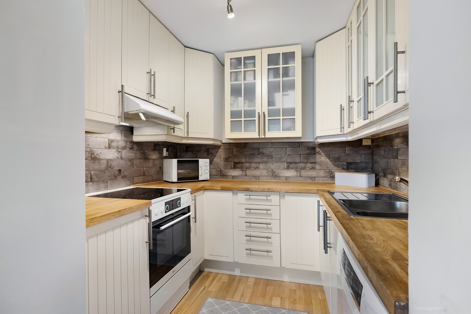 Hvitevarer er frittstående og det er plass til en komfyr, en oppvaskmaskin og kjøl/frys. mellom under og overskap er det montert tapet med mønster som keramiske fliser. Det er montert demping på skuffer. Galleribilde