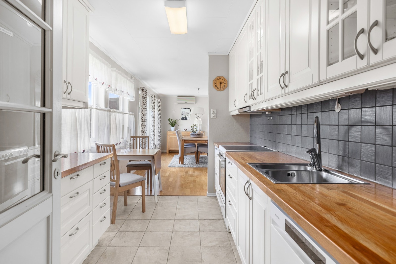 Lyst kjøkken med flislagt gulv, profilerte fronter og heltre benkeplate. Det er også plass til et frokostbord. Galleribilde