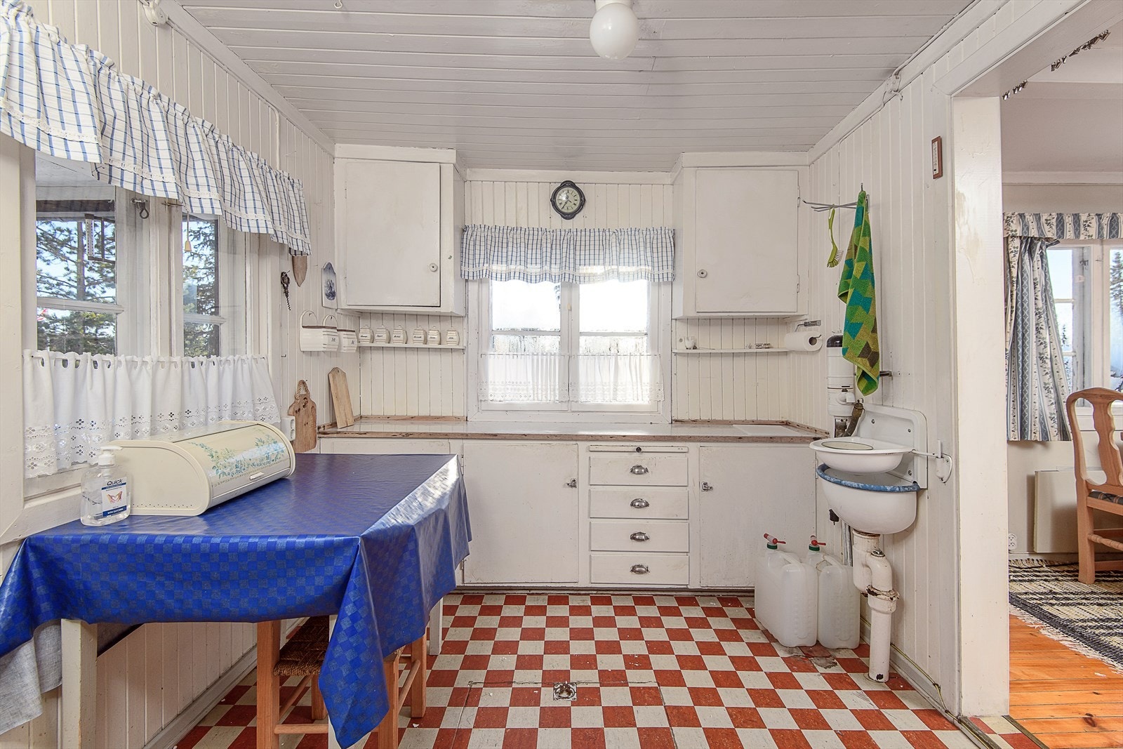 Enkelt eldre kjøkken malt i hvitt. Dører og skuffer for oppbevaring. Utslagsvask og plass til kjøkkenbord. Galleribilde