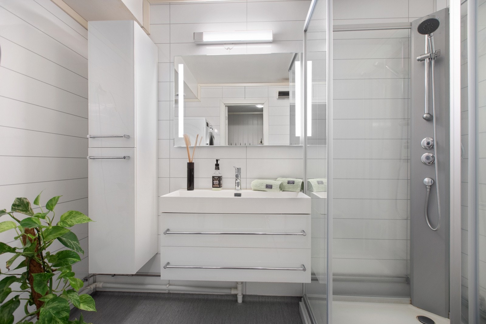 Praktisk innredet bad med bred servant med skuffer. Speil med integrert belysning og høyskap. Galleribilde