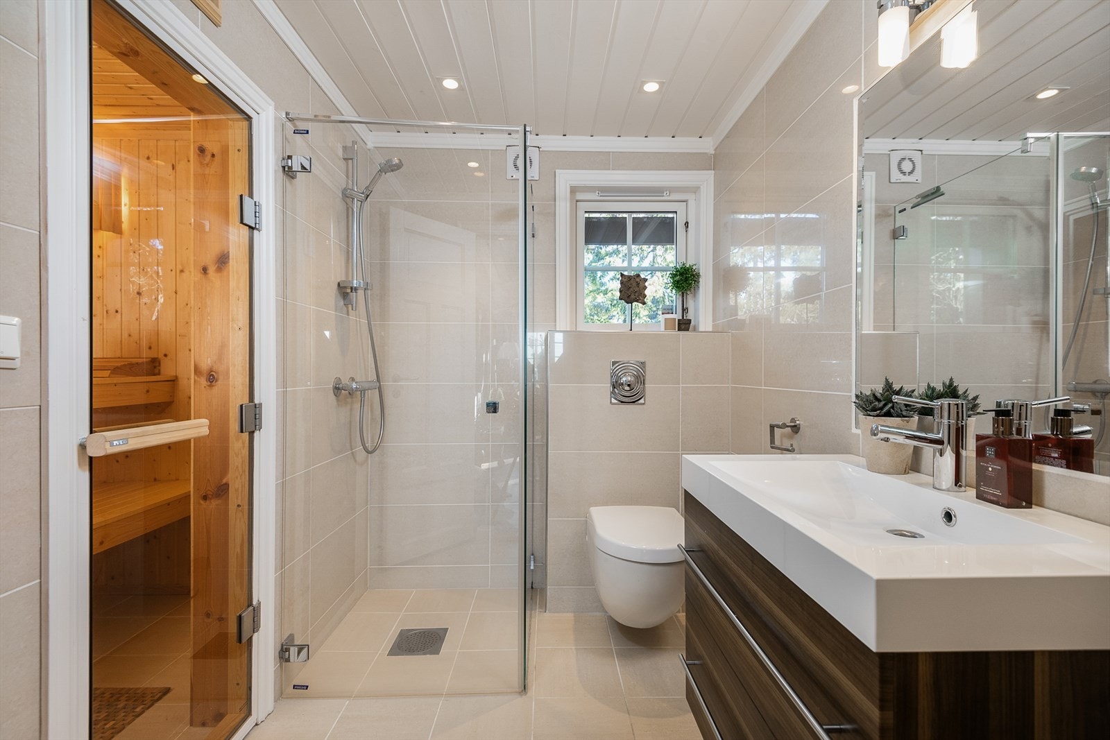 Delikat og innbydende hovedbad har lyse fliser på gulv og vegger. Vegghengt WC, servantinnredning og dusjhjørne med glassdører. Galleribilde