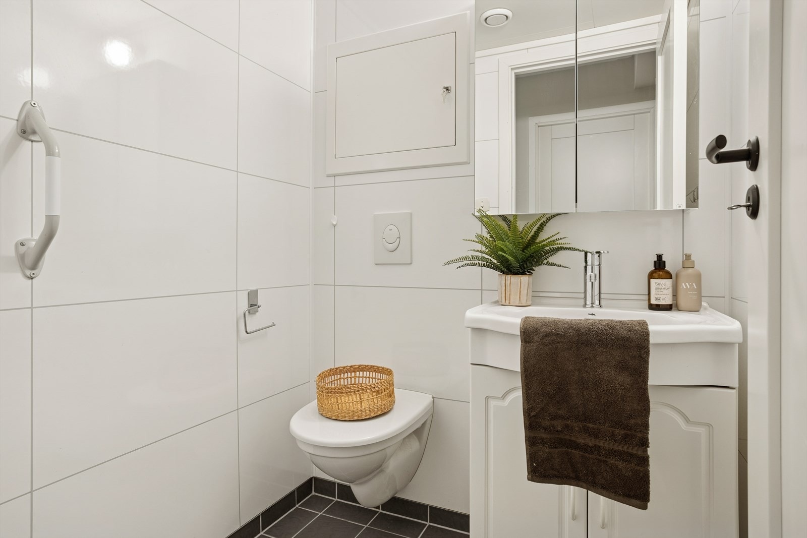 Toalettrommet har fliser på gulv og baderomsplater på vegger, med vegghengt toalett og benkeskap. Galleribilde