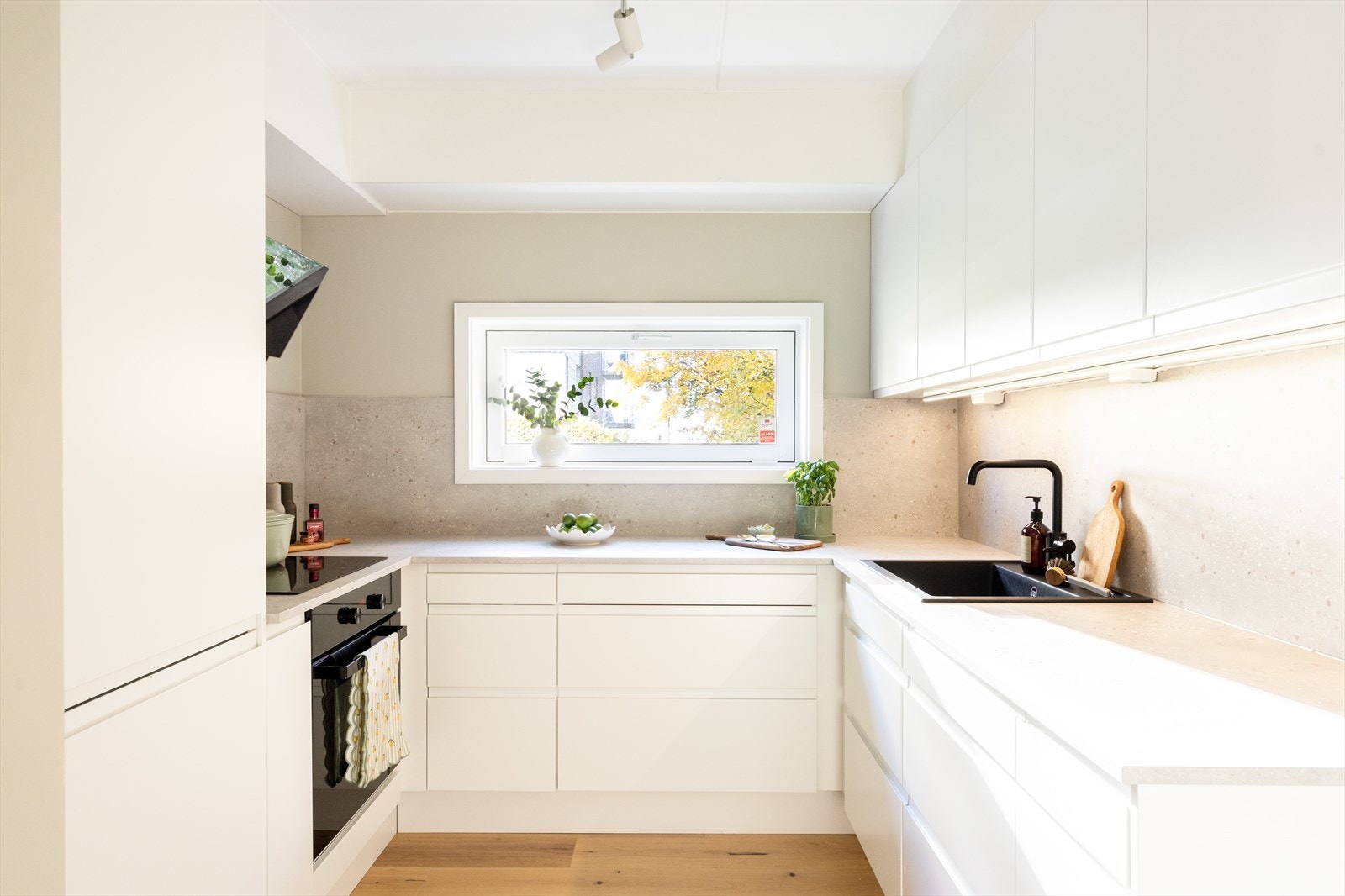 Stilrent kjøkken fra 2023 hvor kjøkkeninnredningen består av hvite, glatte fronter og benkeplate av laminat med nedfelt vaskekum. Galleribilde