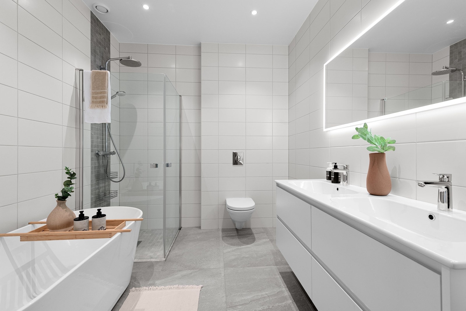 Flott flislagt bad med stor baderomsinnredning med skuffer og 2 servanter med ett-greps armatur. Dusjhjørne med glassvegger og vegghengt dusjarmatur med hånddusj og regndusj. Frittstående badekar og vegghengt toalett Galleribilde