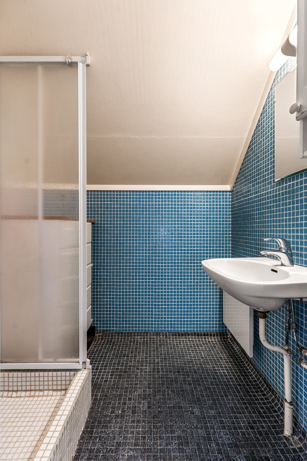 Baderom med flislagte gulv og vegger. Dusjnisje og servant, samt muliget for oppbevaring i benk. Galleribilde