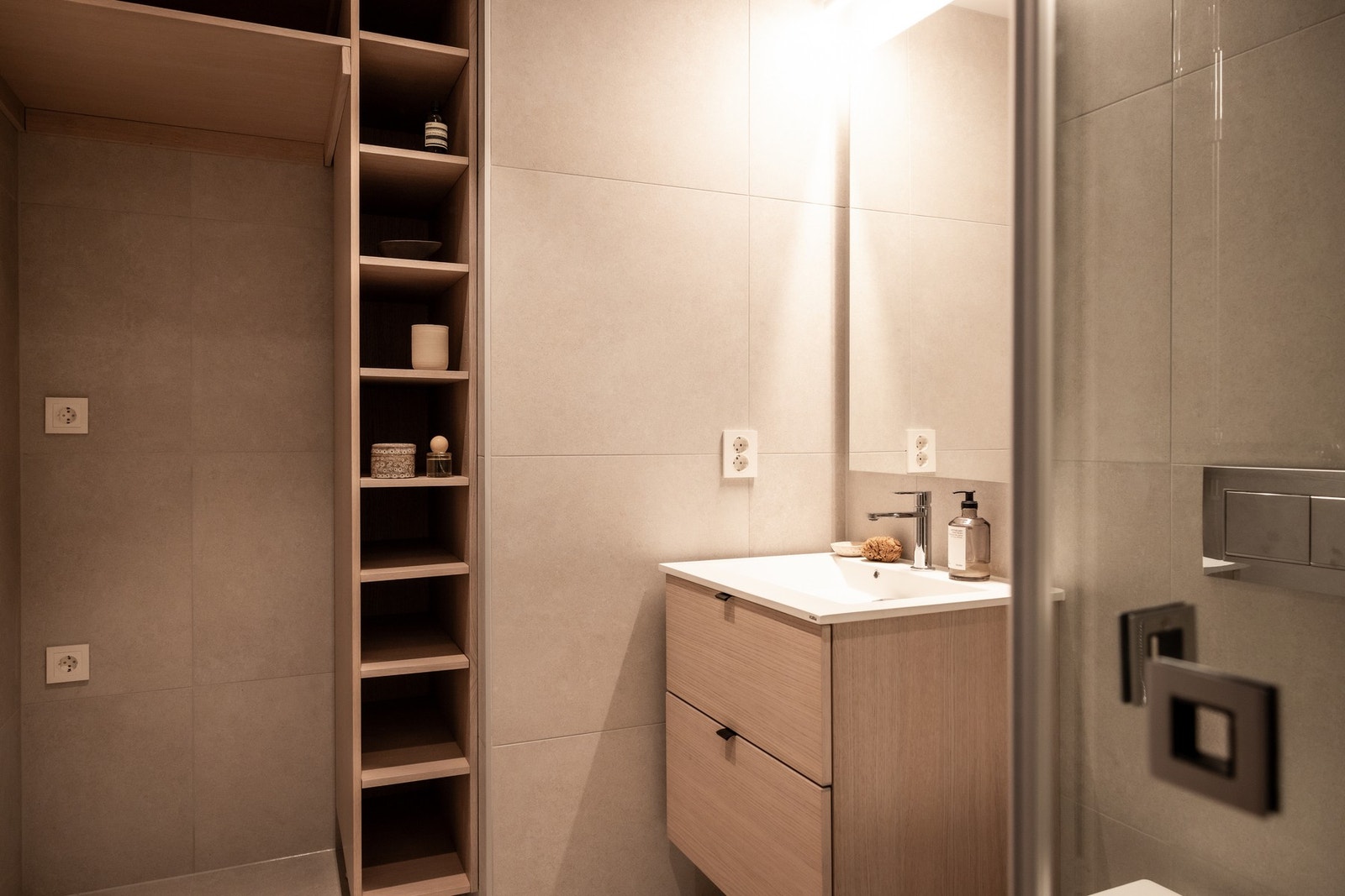 Rommet er innredet med vegghengt servantinnredning med skuffer og ovenpåliggende servant, speil med overlys og stikkontakt, dusjhjørne med glassdører samt veggmontert dusjarmatur med både hånddusj og regndusj. Galleribilde