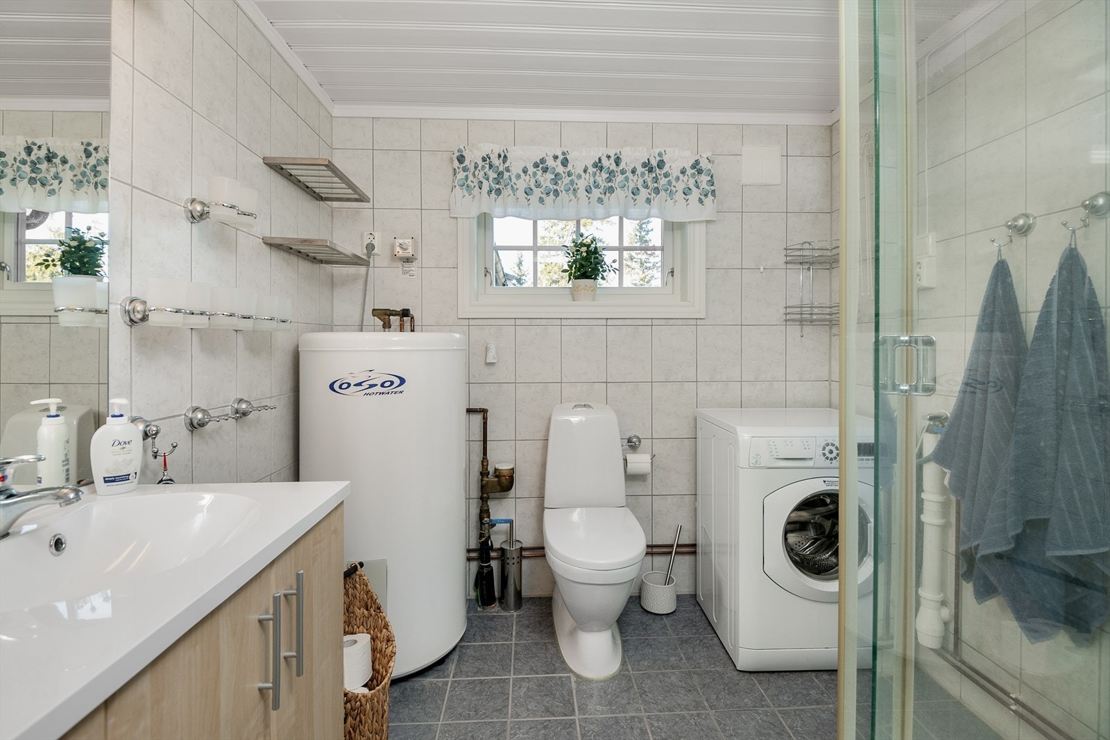 Flislagt bad/wc har dusj og servantinnredneing, samt opplegg for vaskemaskin og varmtvannsbereder. Galleribilde