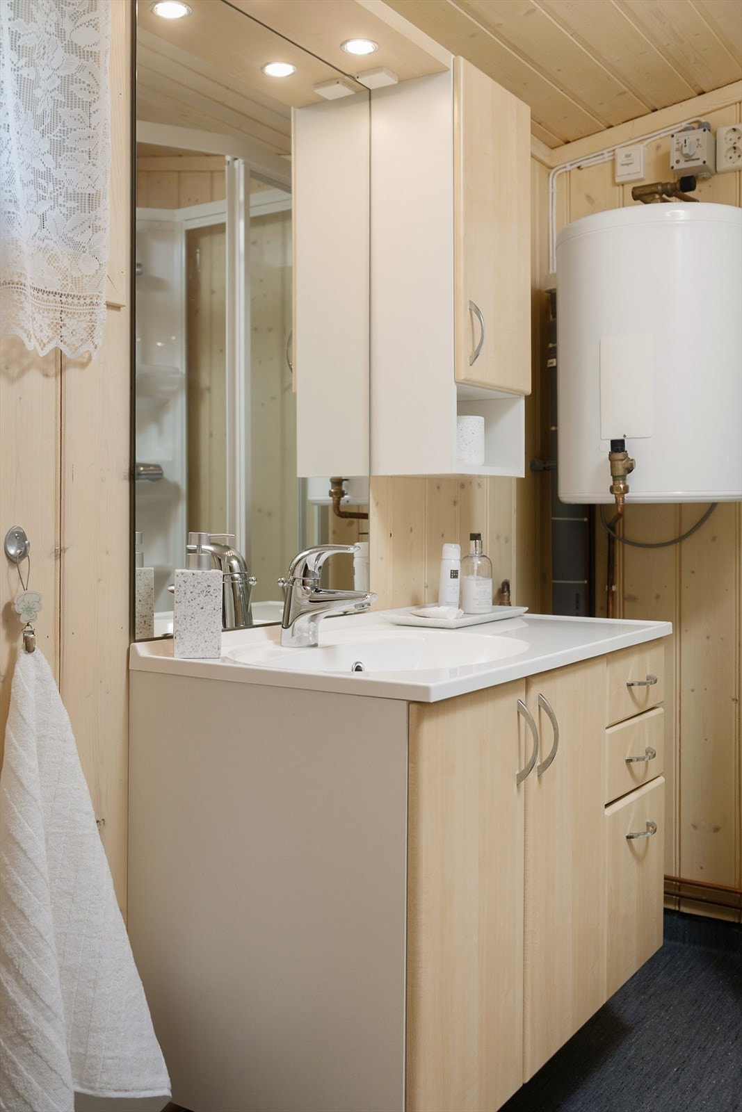 God oppbevaring i servantinnredningen med skap og skuffer. Overskap og speil. Vegghengt varmtvannsbereder er plassert på badet. Galleribilde