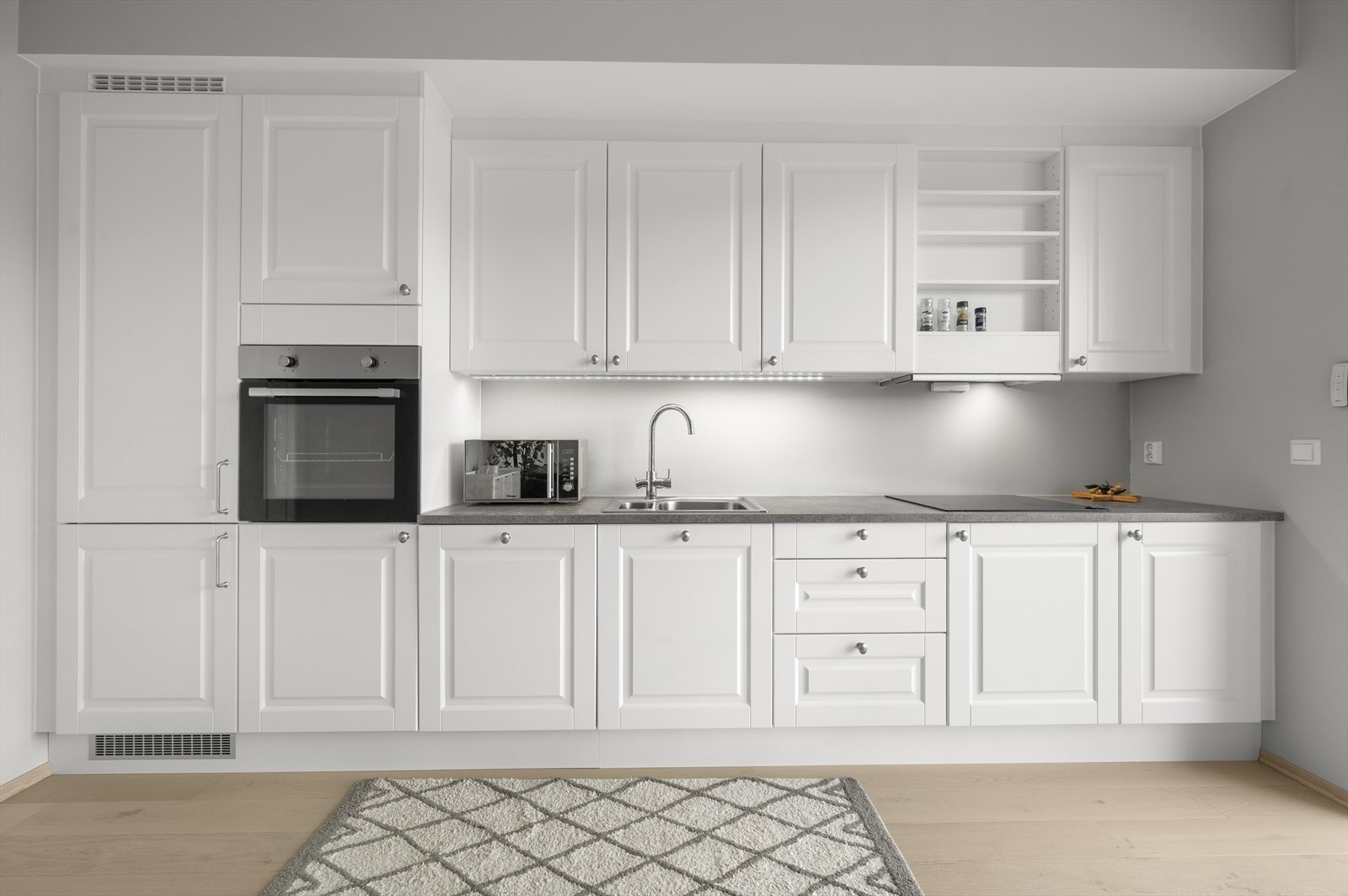 Kjøkken innredning har profilerte fronter, integrerte hvitevarer som oppvaskmaskin, platetopp, stekeovn i høyskap og komfyrvakt. Det er kjøkkenventilator med avtrekk ut. Galleribilde