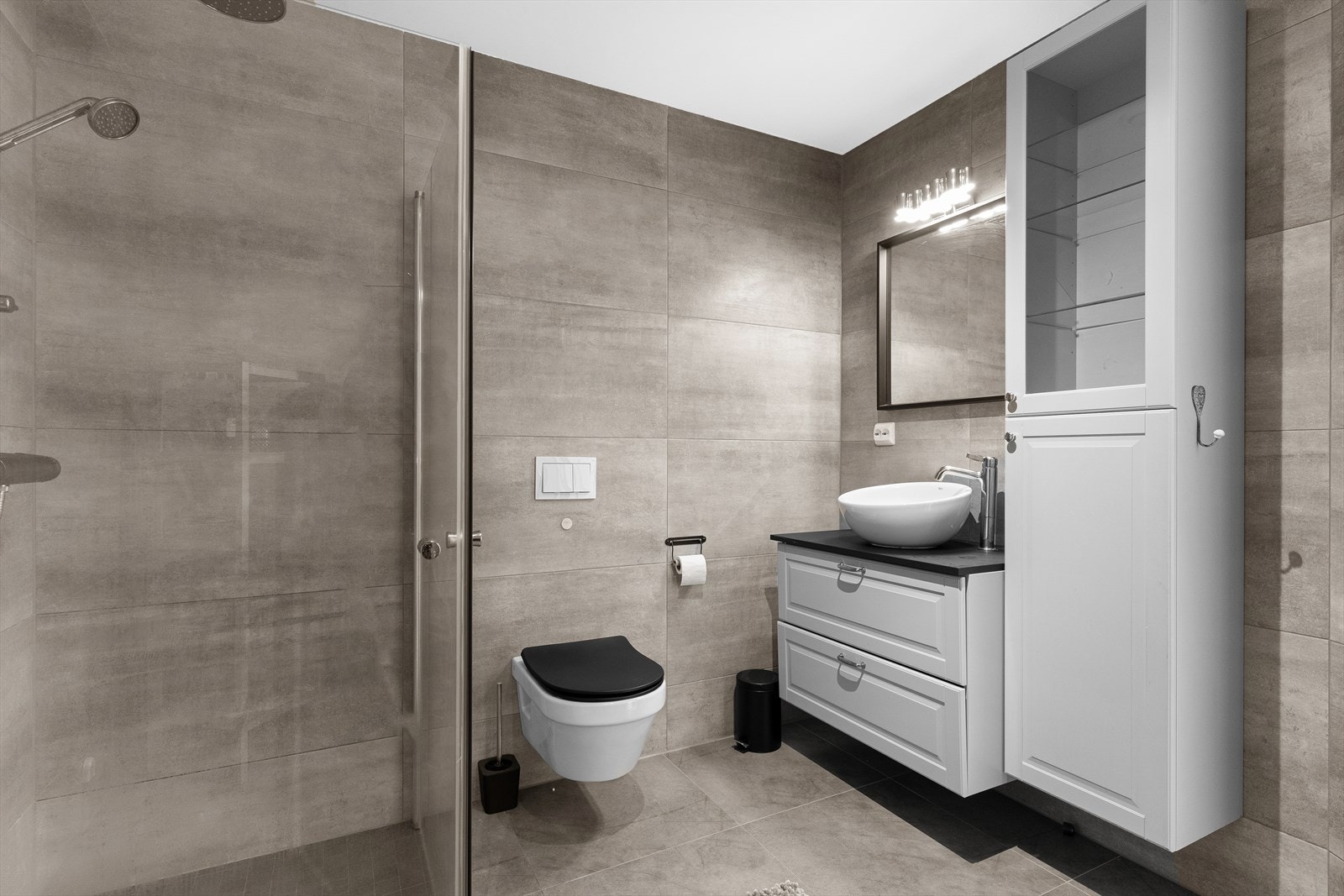 Badet er innredet med baderomsinnredning med bolleservant med oppbevaring, speil, vegghengt toalett og dusjhjørne med regndusjarmatur. Galleribilde