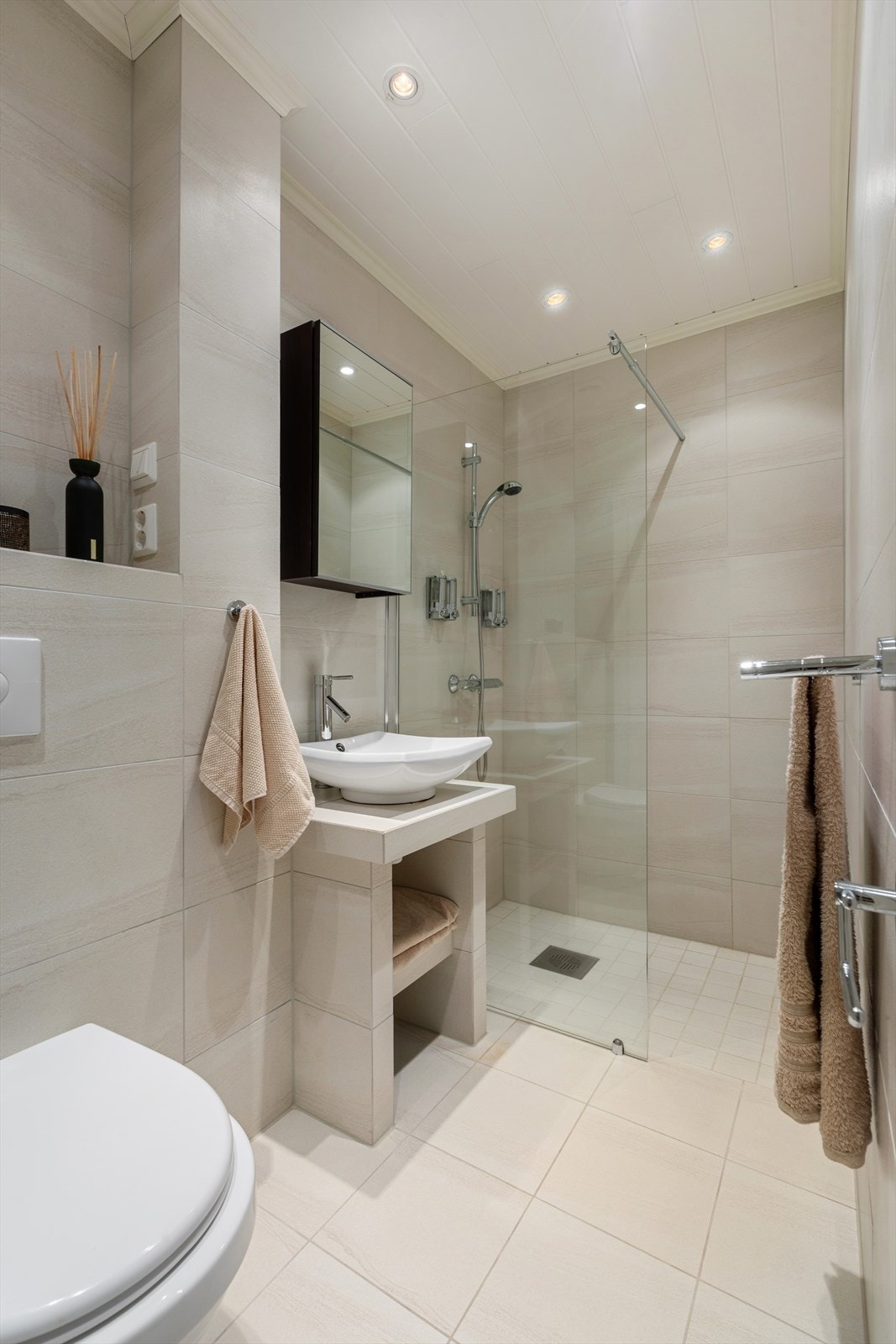 Moderne, pent flislagt bad med stilren innredning bestående av vegghengt klosett, dusjhjørne og servantinnredning med speilskap Galleribilde