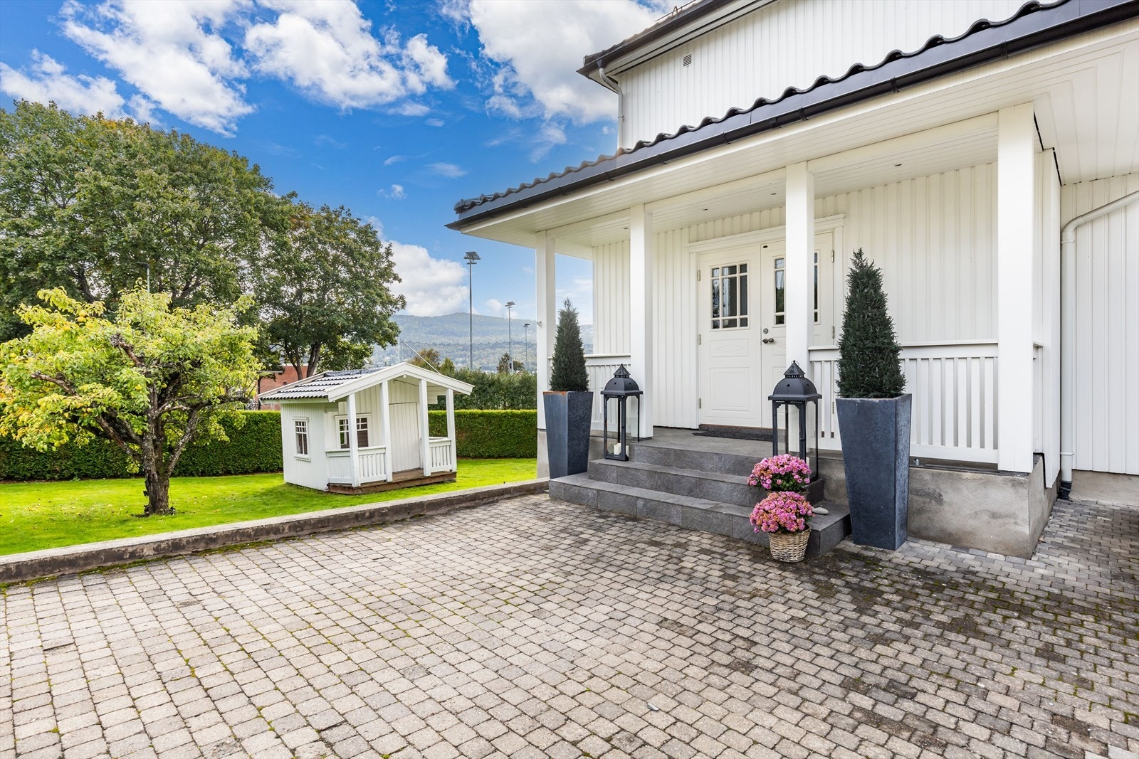 Pent opparbeidet tomt med beplantning, hekk og gressplen. Det er steinbelagt gårdsplass Galleribilde
