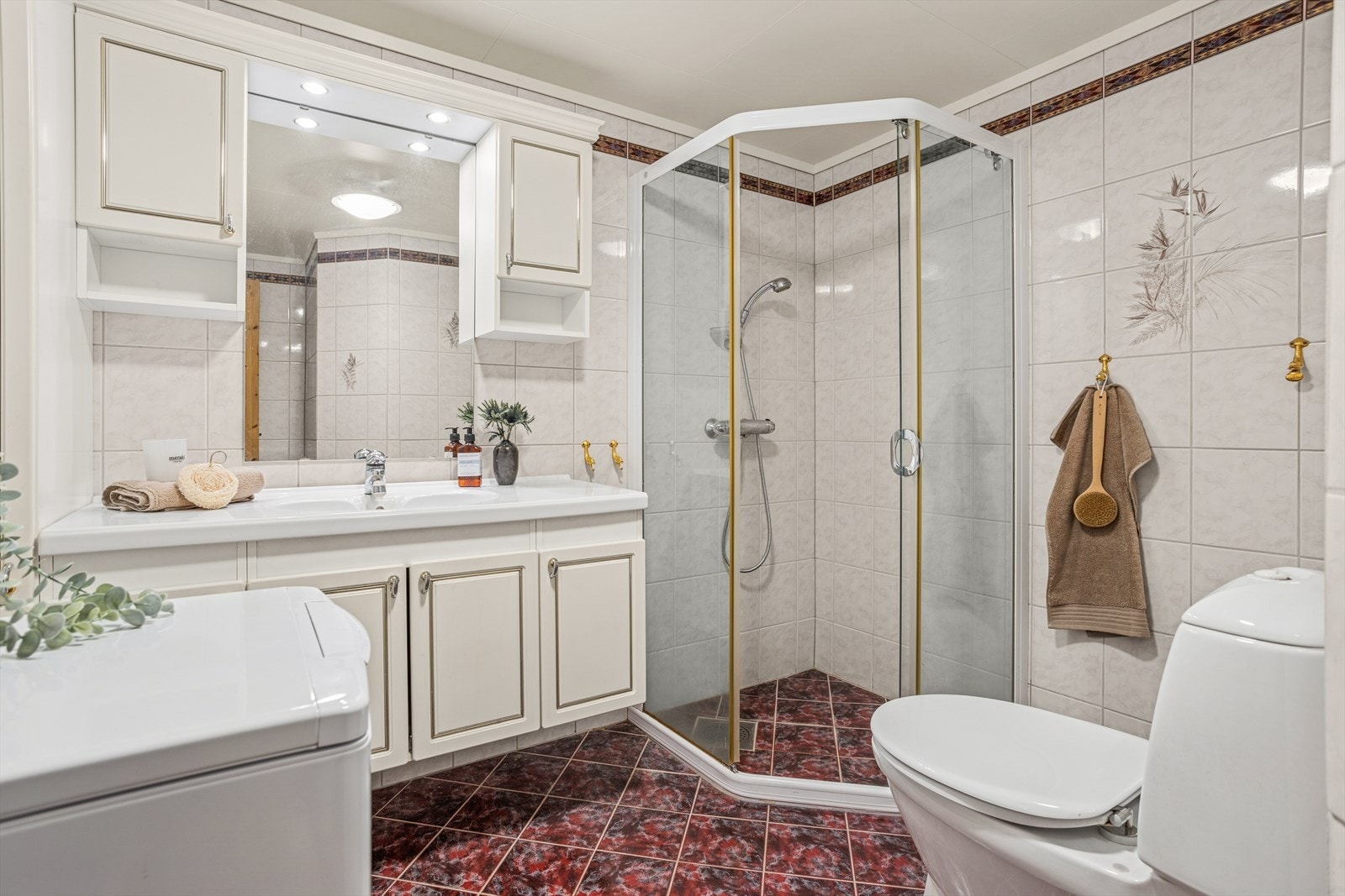 Lyst flislagt bad utstyrt med dusjhjørne, gulvstående toalett og opplegg for vaskemaskin. Galleribilde