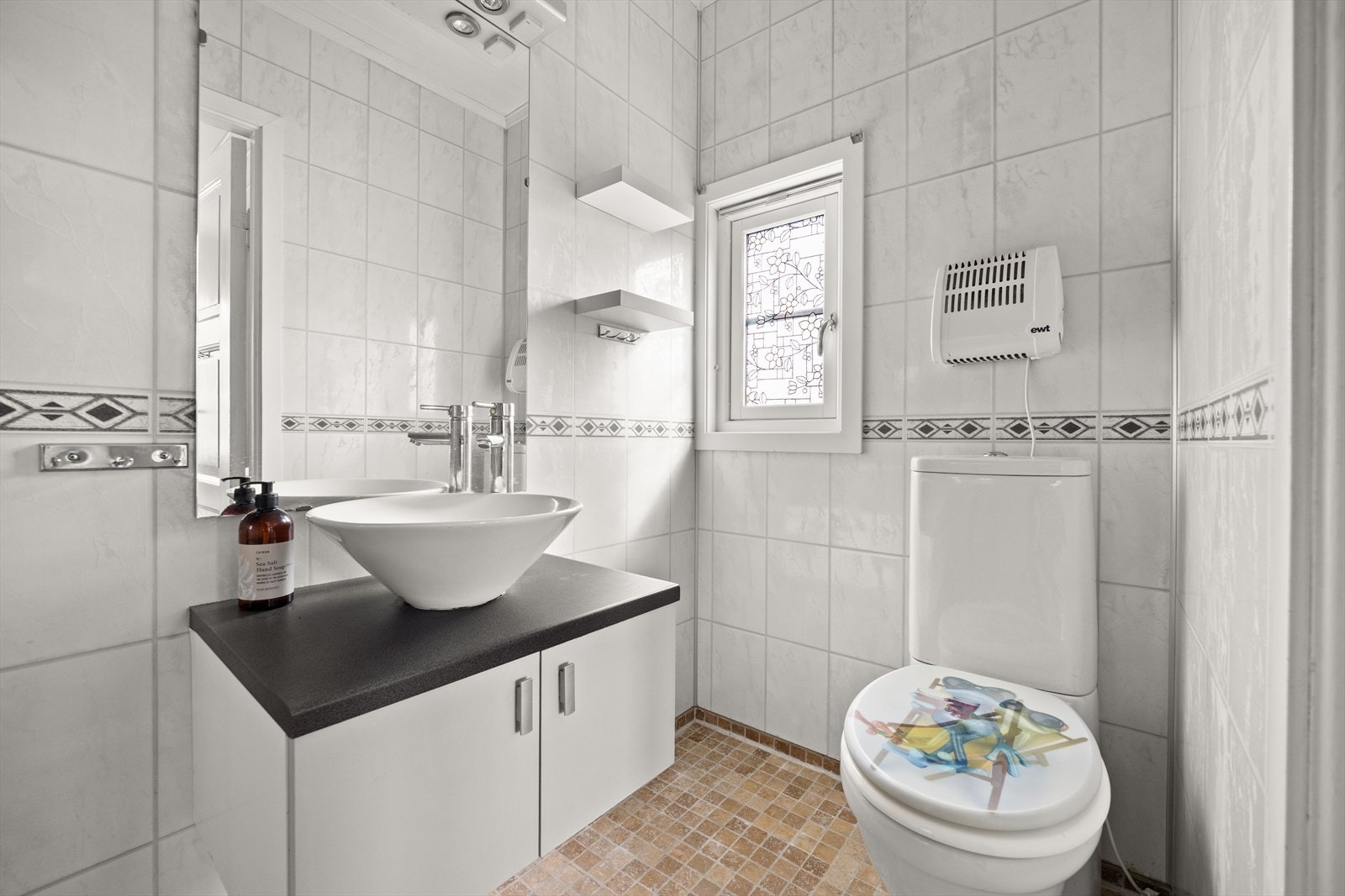 Flislagt bad med toalett, servant i innredning, dusj og lyssatt speil Galleribilde