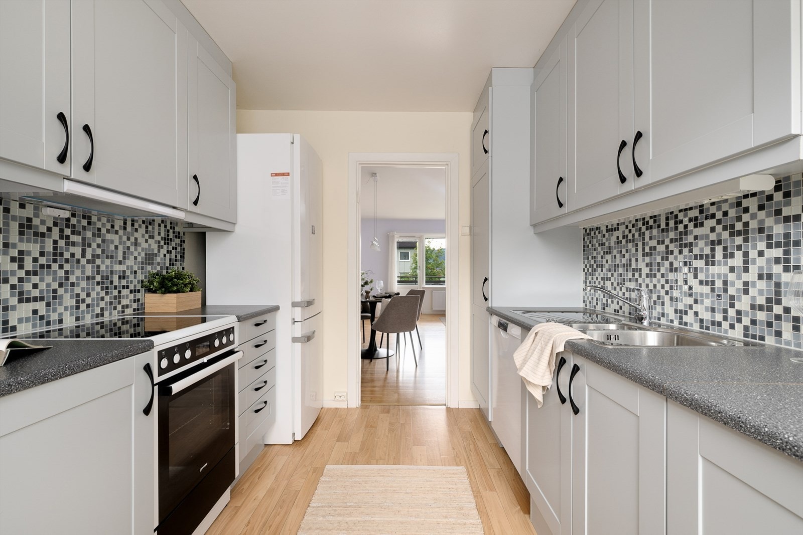 Kjøkkenet har innredning med lyse grå fronter med enkel profilering og fliser mellom benkeplate og overskap. Galleribilde