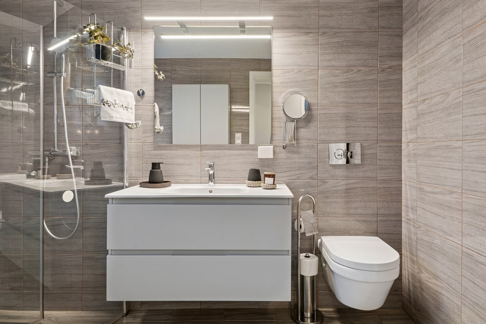 Badet fremstår som både elegant og funksjonelt, med gråbeige fliser på vegger og gulv som gir et tidløst og stilrent uttrykk Galleribilde