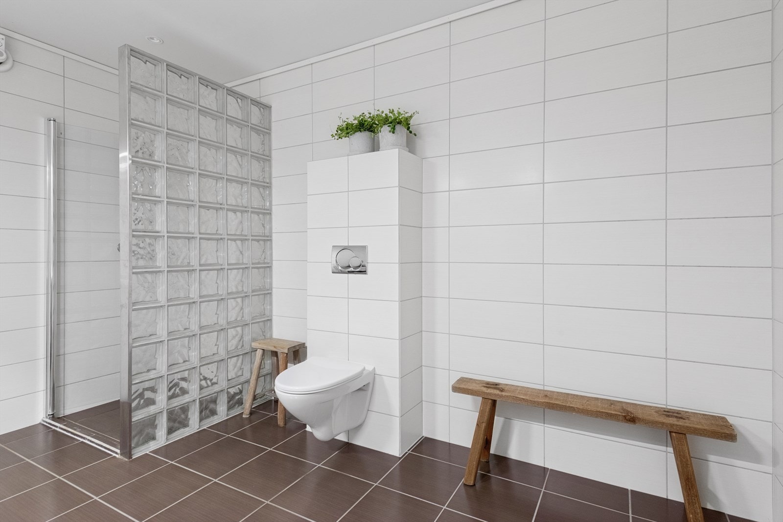 Vegghengt toalett og glassbyggerstein mot dusjsone skaper et moderne uttrykk. Galleribilde