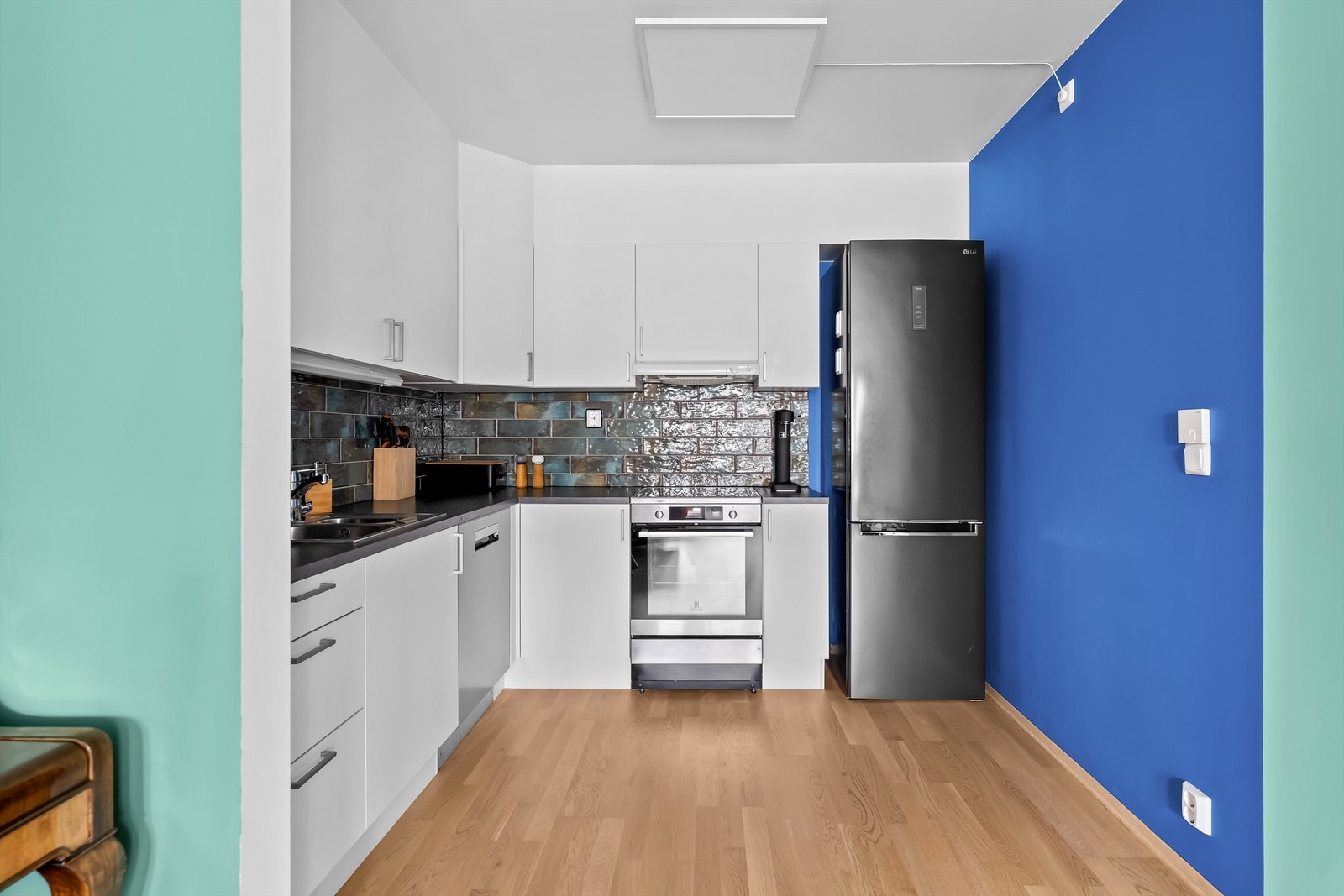 Overskap har belysning under og ventilator er tilkoblet avtrekkskanal. Det er laminert benkeplate med skyllekum og oppvaskkum med ett-greps armatur, og fliser over benkeplate. Galleribilde