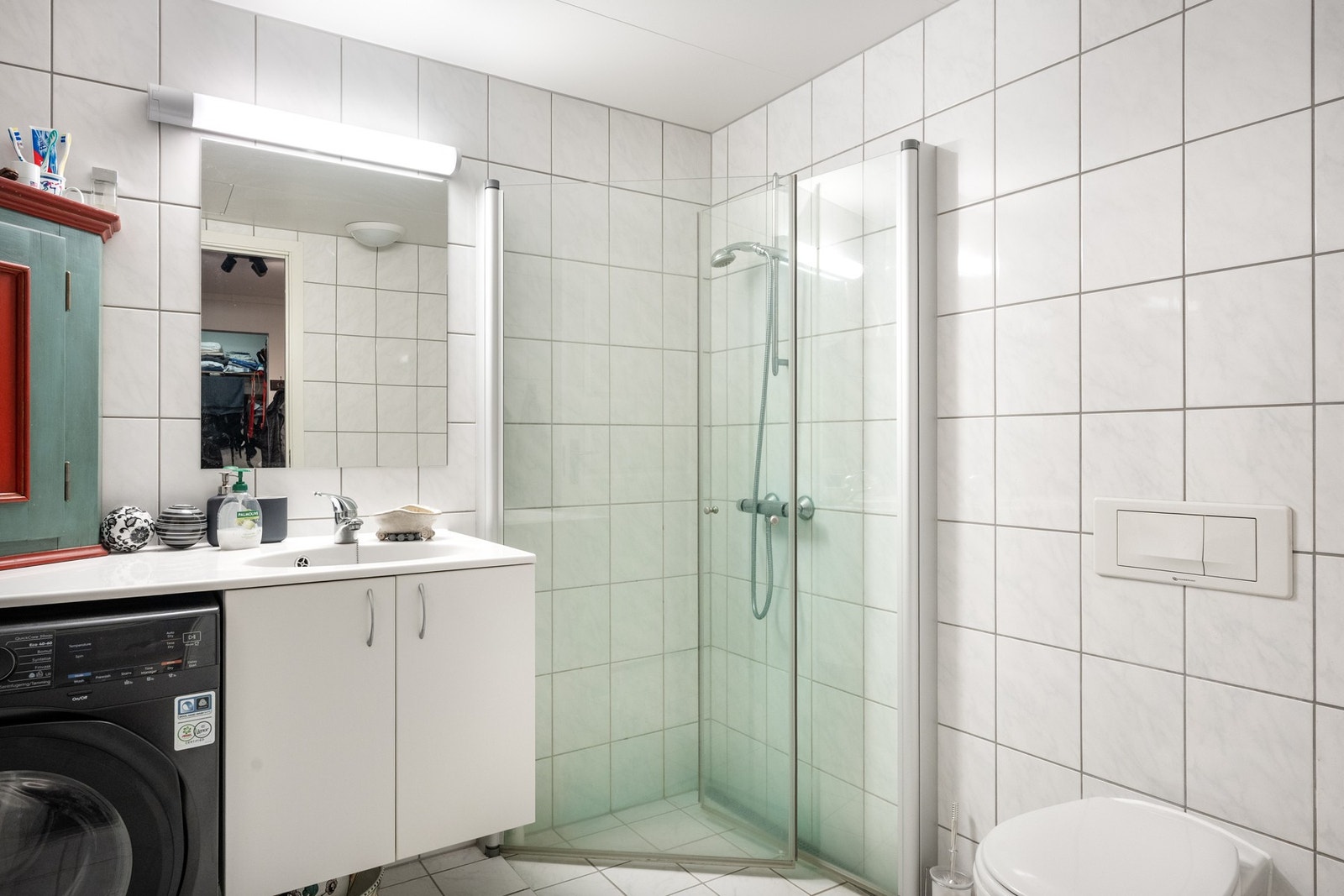 Hovedbadet, med adkomst fra entré, er romslig og har støpte gulv med varme og helflisede gulv og vegger. Her er det innredet med veggmontert vannklosett, dusjnisje og heldekkende servantplate hvor opplegg og rom til vaskemaskin fint er plassert under for Galleribilde