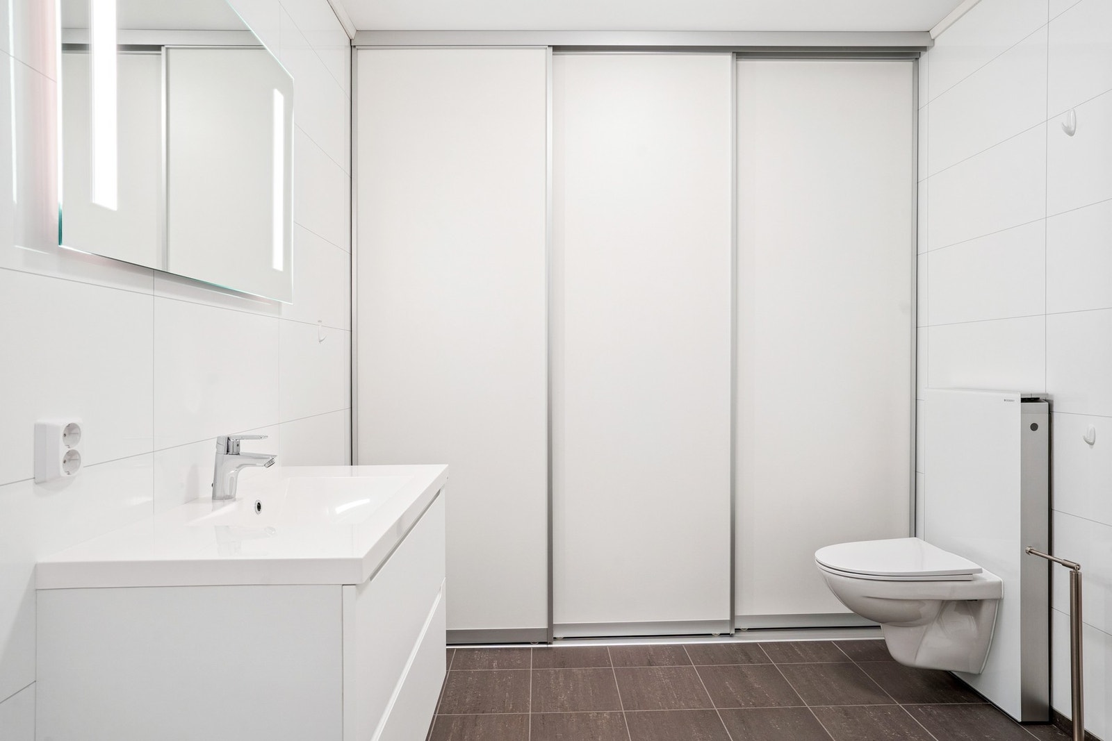 Badet er innredet med vegghengt toalett, servant på møbel, dusjhjørnet og skyvedørsgarderobe. Galleribilde