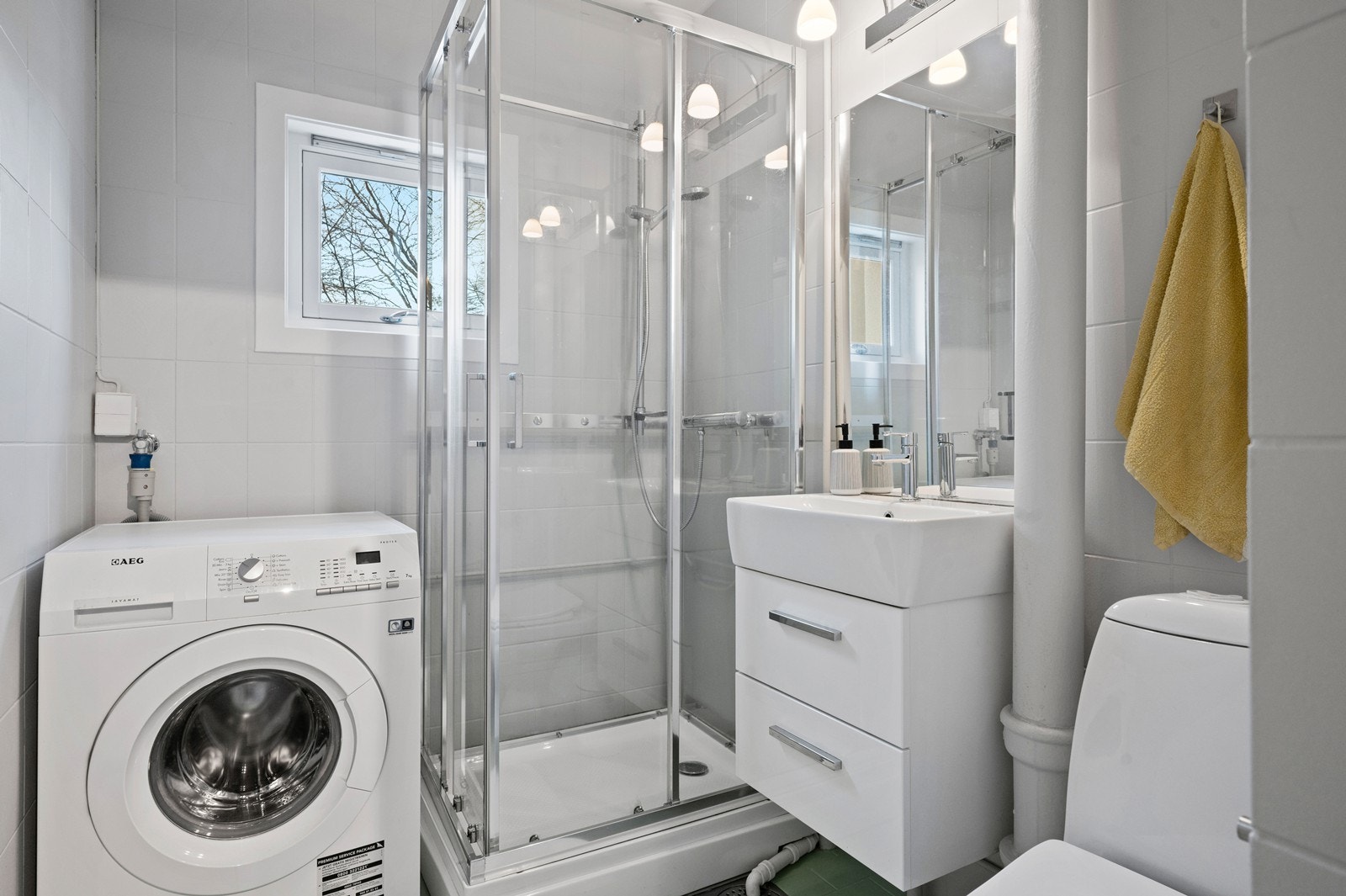 Flislagt bad med dusjkabinett og praktisk opplegg for vaskemaskin. Galleribilde