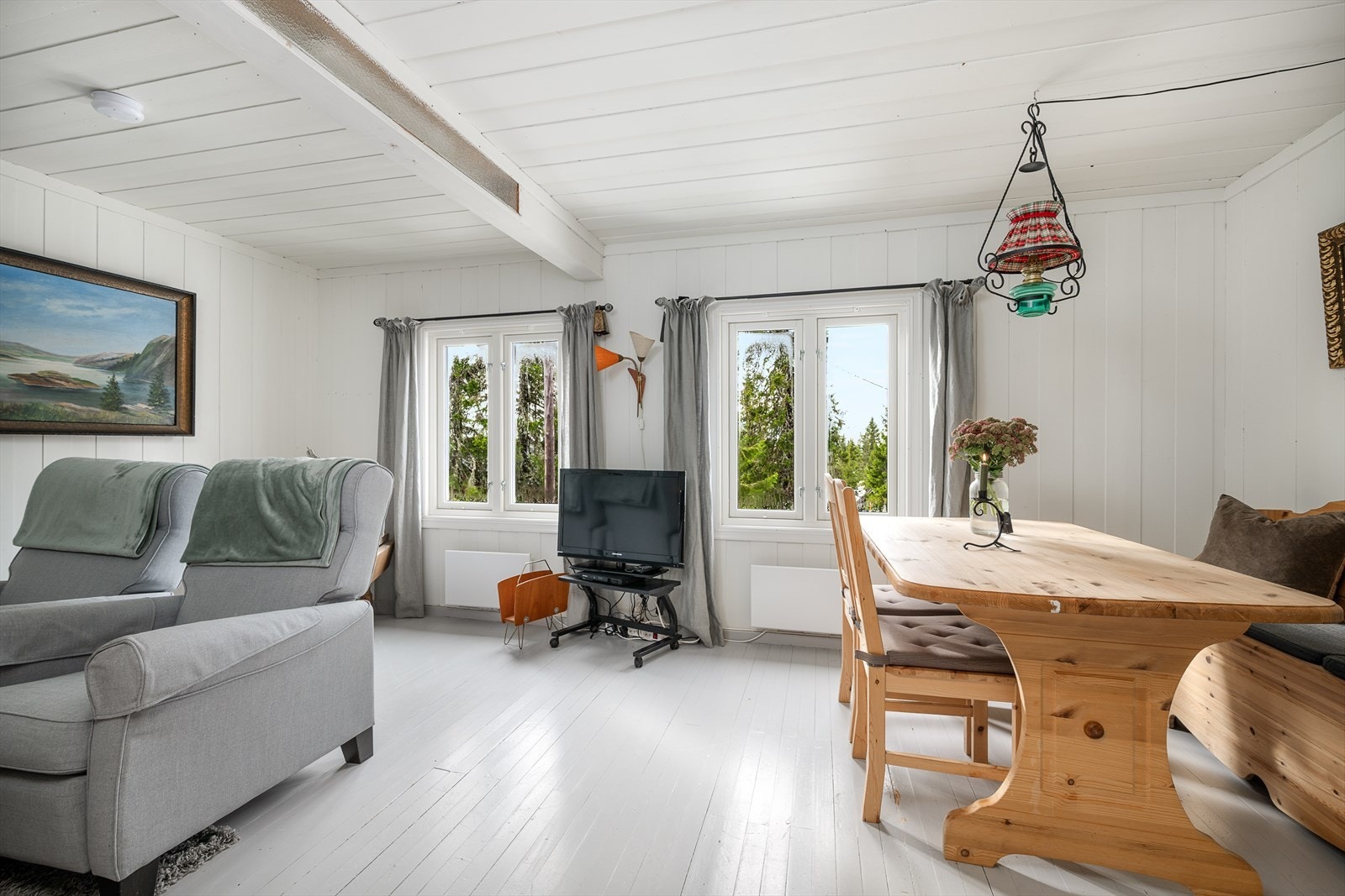 Stua har overflater i lyse og tidløse fargteoner. Eldre hytte der den opprinnelige panelen og tregulvet er malt. Galleribilde