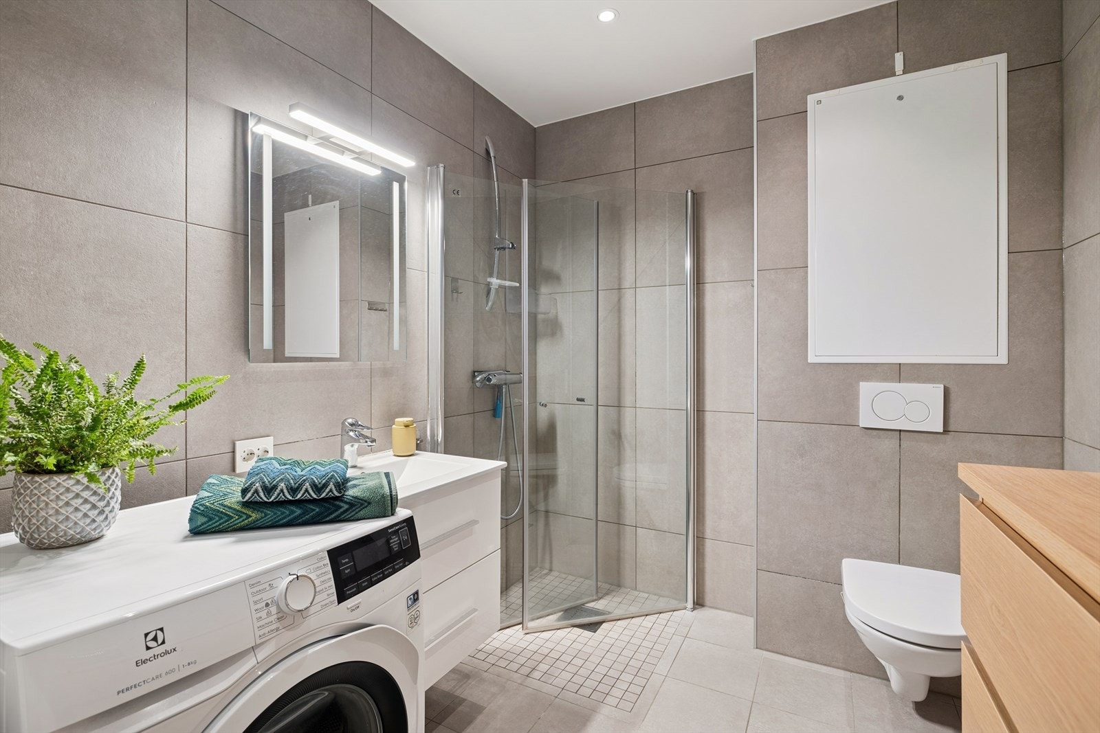 Moderne flislagt bad med gulvvarme som gir komfort og holdbarhet. Dusjhjørne med foldedører og vegghengt klosett kompletterer det funksjonelle baderommet. Downlights og opplegg for vaskemaskin. Galleribilde