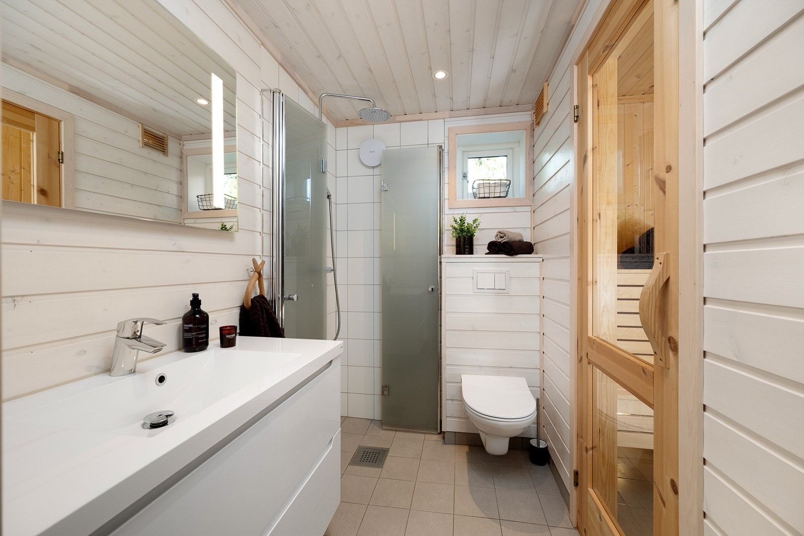 Funksjonelt og tidløst baderom har vegghengt WC, dusj og baderomsinnredning. Adkomst til badstue. Galleribilde