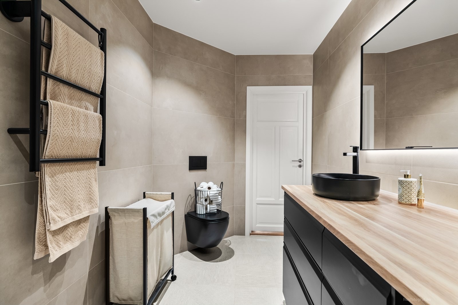 Rommet er flislagt og har elektriske varmekabler i gulvet, og det er innredet med servant i møbel, høyskap, veggmontert toalett, dusjhjørne med glassvegger og opplegg for vaskemaskin. Galleribilde