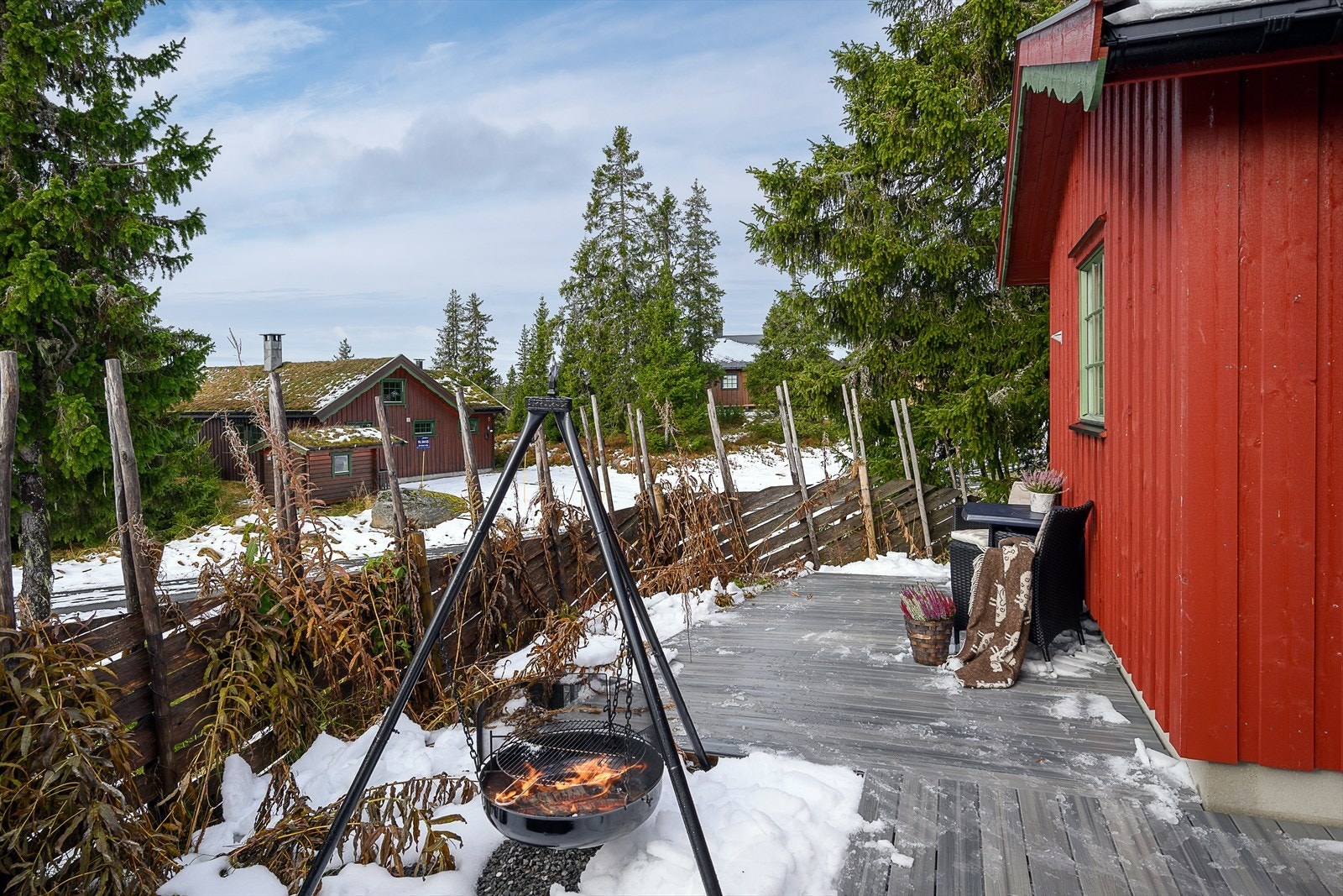 Hyggelig bålplass på terrassen mellom hytta og garasjen. Deler av tomten er inngjerdet med skigard. Galleribilde