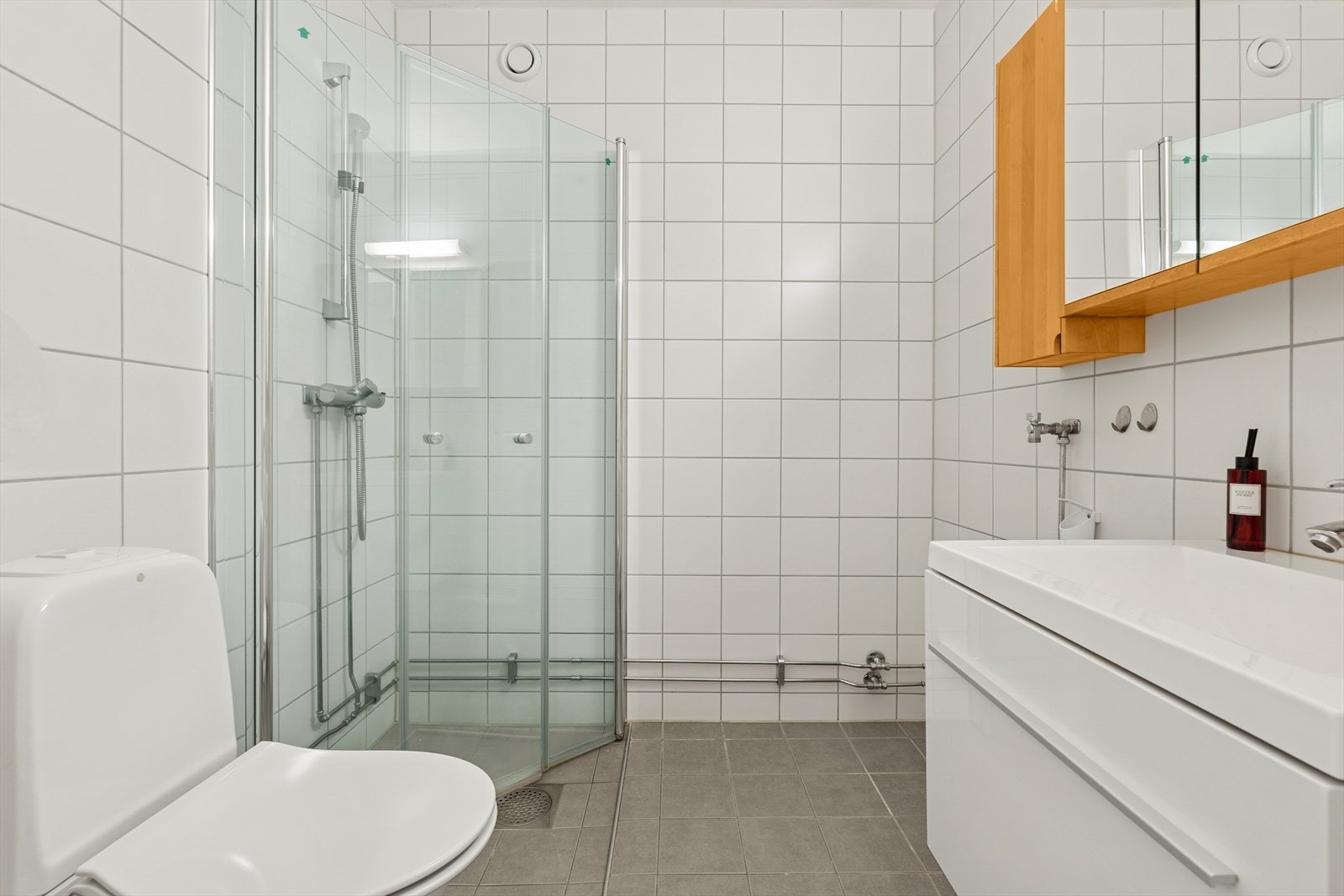 Badet er innredet med dusj med innfellbare glassfører, servant med innredning, speil med belysning og klosett Galleribilde