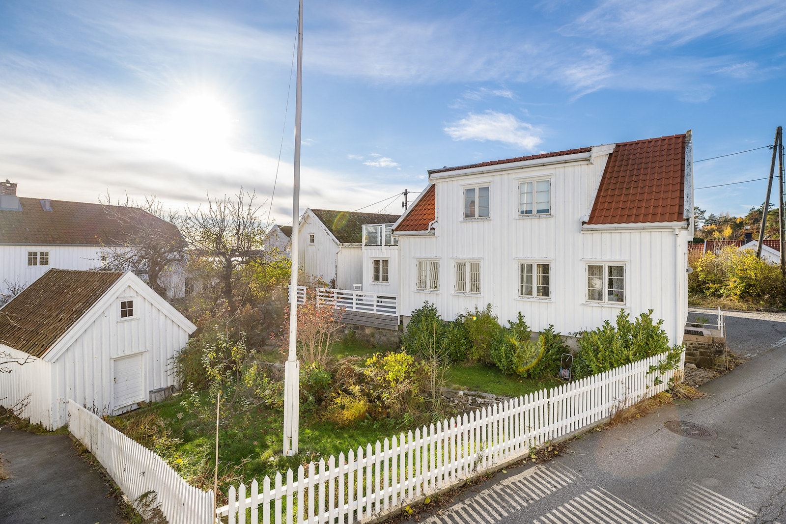 En inngjerdet hage er opparbeidet med flaggstang, variert beplantning og en stor utebod over to plan. Galleribilde