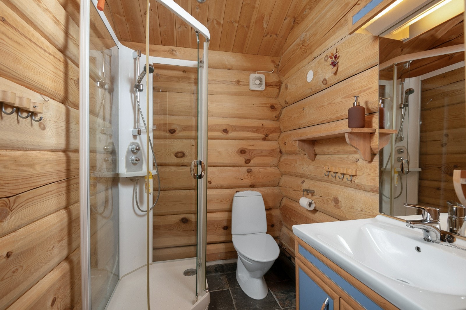 Det andre baderommet er også beliggende i første etasje, er med fliselagte overflater på gulv og tømmer på vegger. Videre er rommet innredet med baderomsinnredning med servant. speil med tilhørende lys, toalett og dusjkabinett Galleribilde