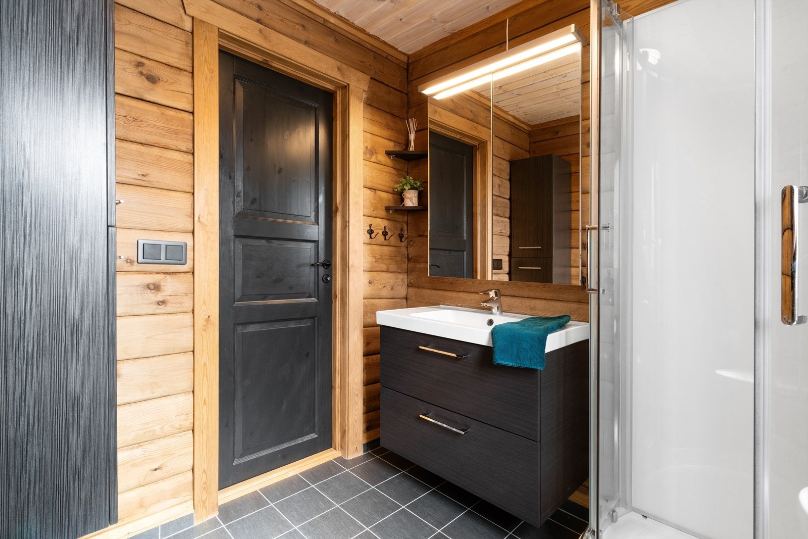 Pent innredet bad med flislagt gulv. Badet har en mørk servantinnredning med nedfelt servant med skuffer og speilskap. Galleribilde