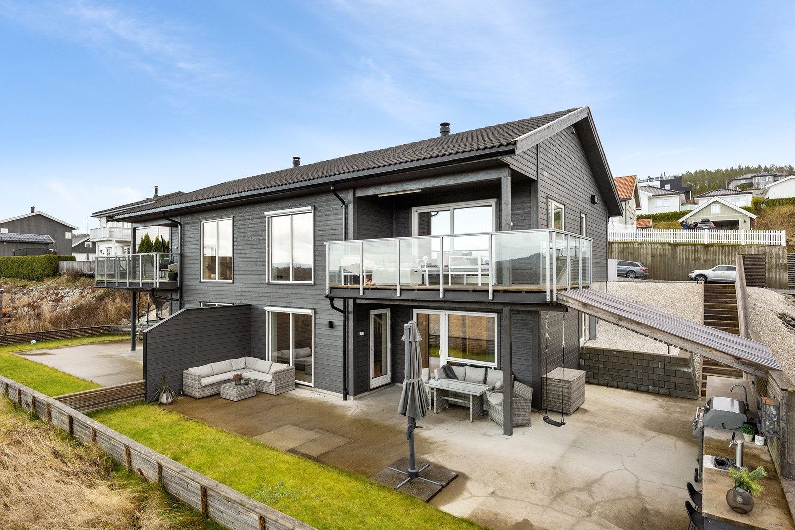 En solid trapp tar deg ned til en inngjerdet hage på nedsiden av huset, opparbeidet med gressplen og markterrasse. Galleribilde